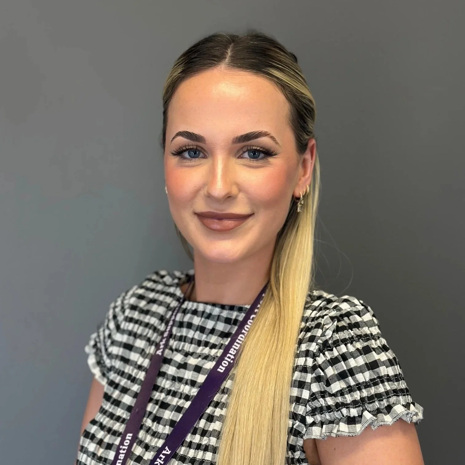A headshot of Faye smiling. Faye has a fringe and is wearing a black top.
