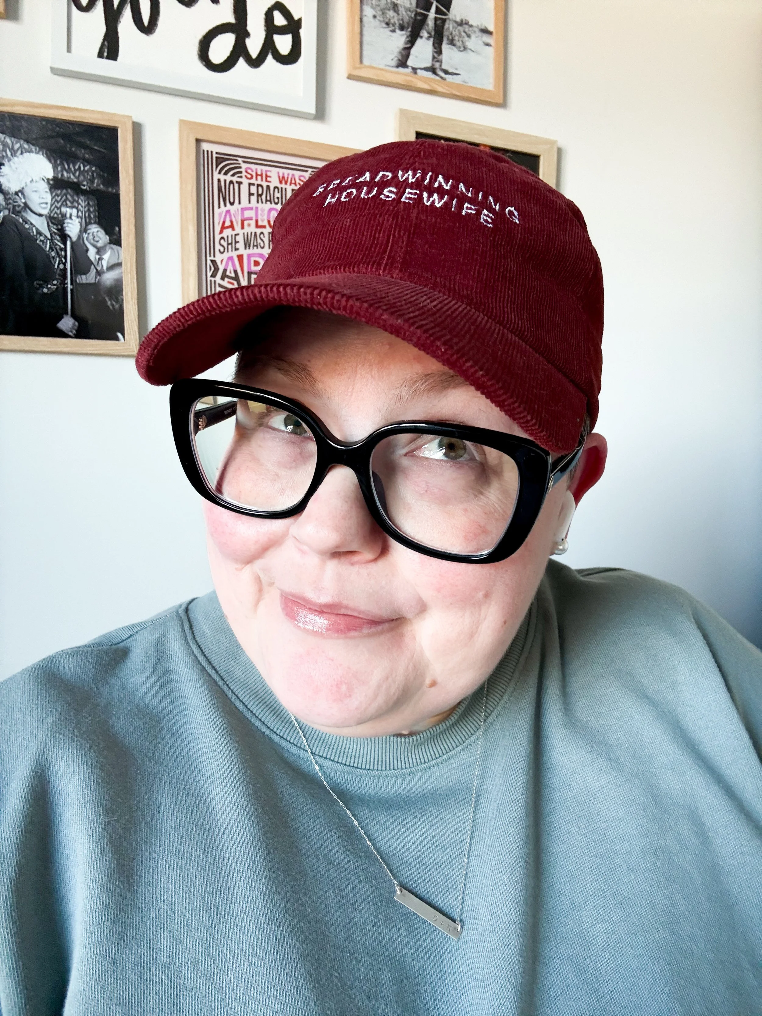 Portrait of Karen Hammons wearing oversized black glasses and a burgundy cap that reads “Breadwinning Housewife.”