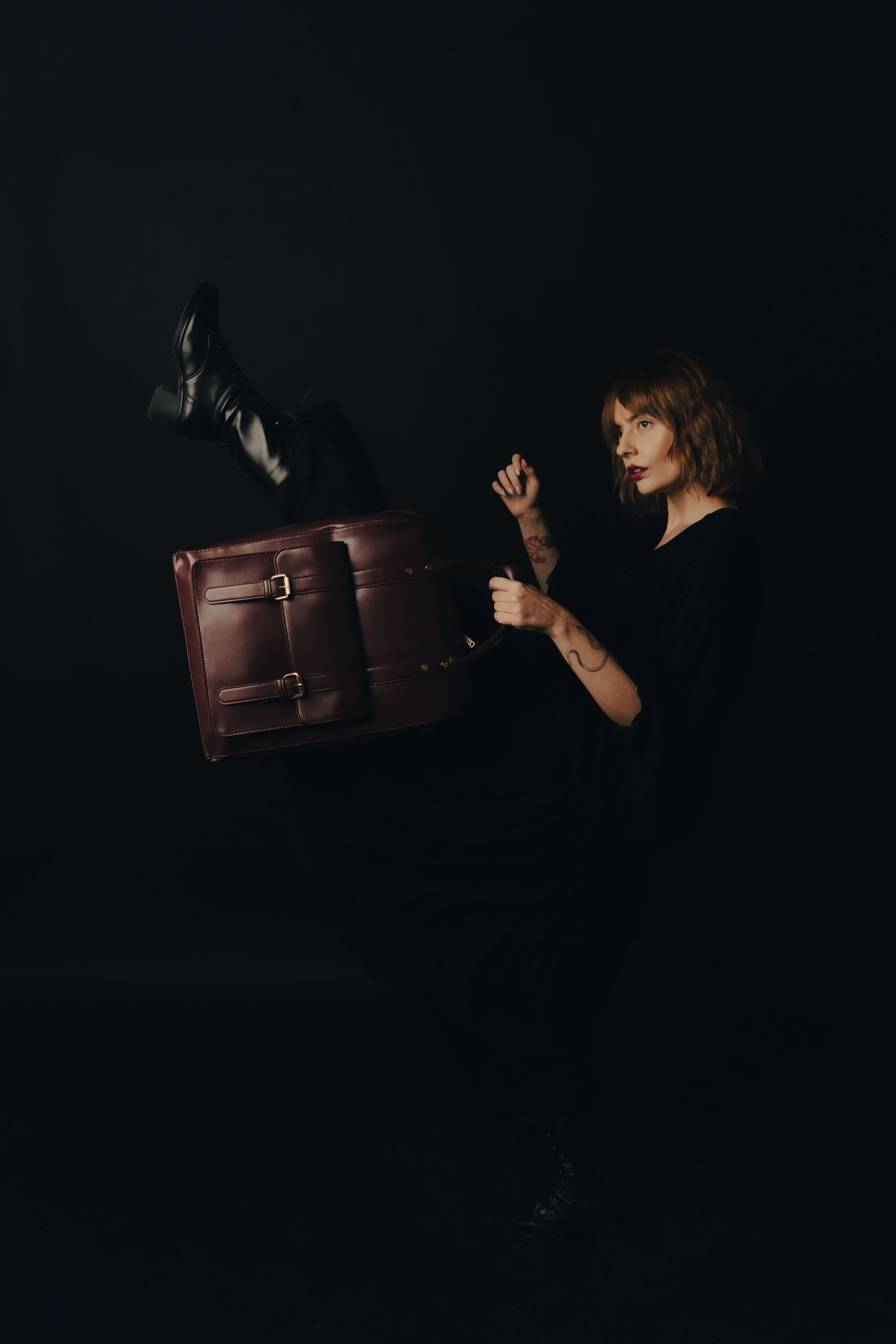 Dark editorial image of a woman dressed in black holding a burgundy leather briefcase.