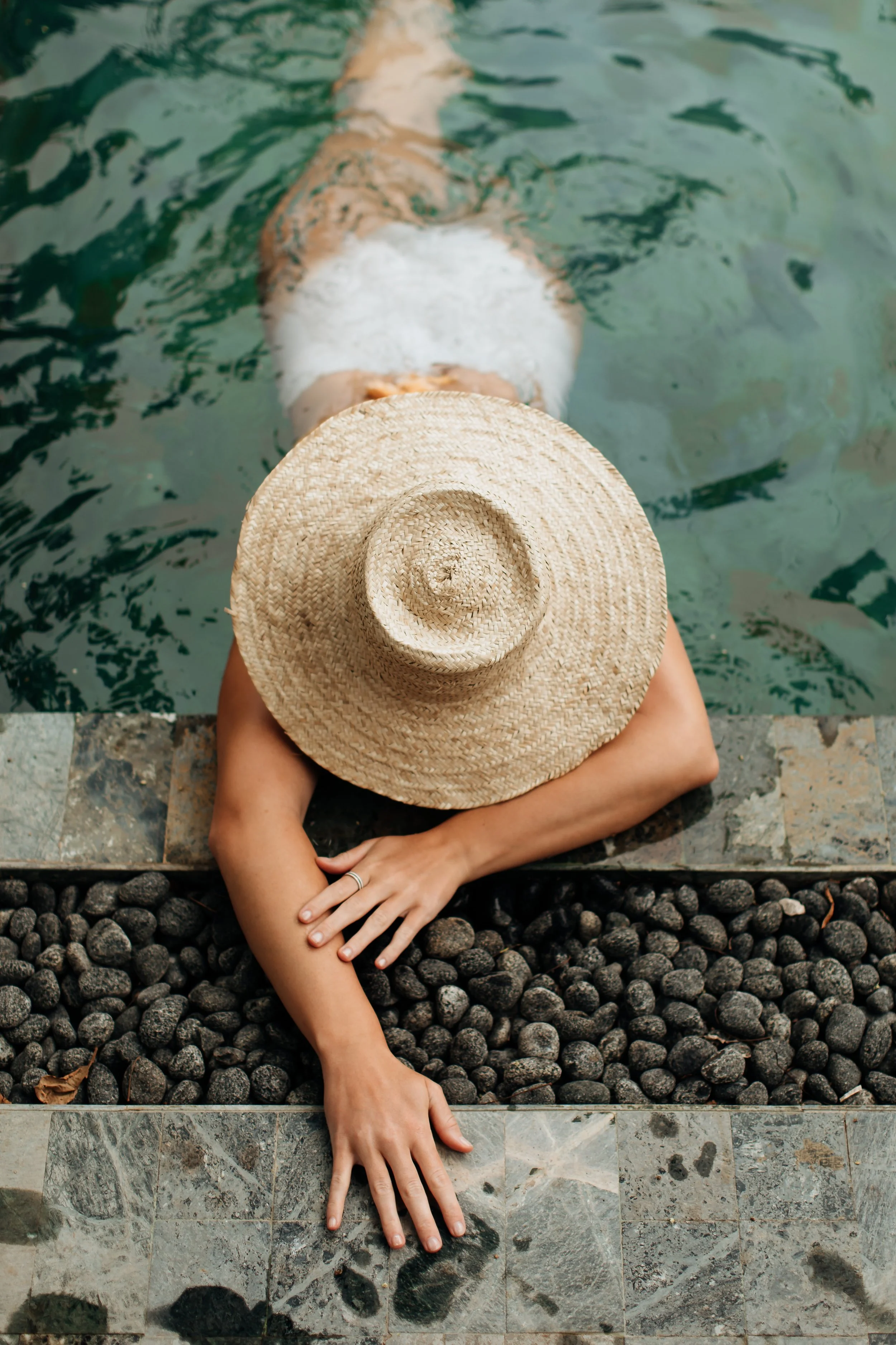 Woman in a wide-brimmed straw hat floating at the edge of a pool.