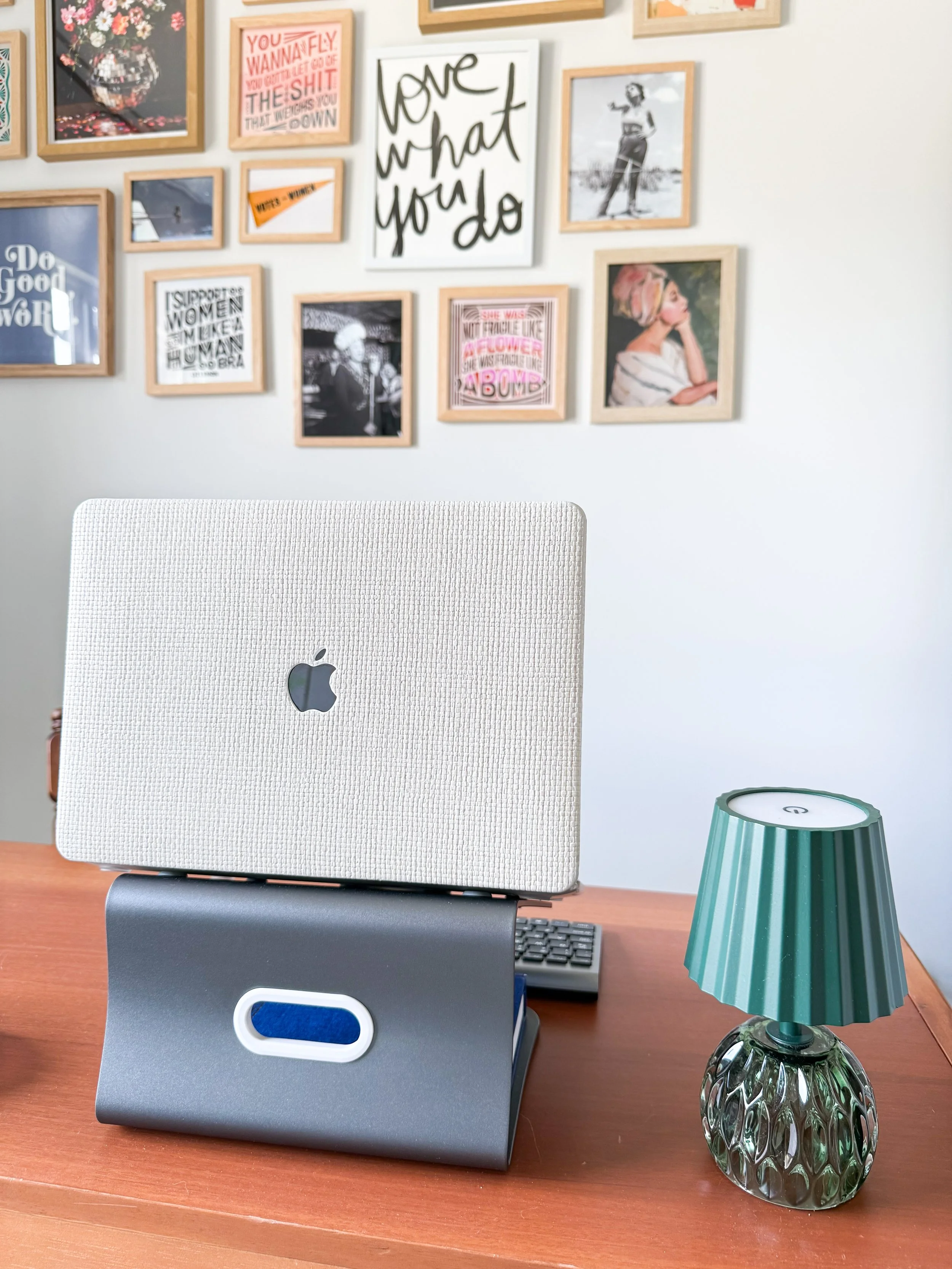 Home workspace with laptop, framed art, and a small green table lamp.