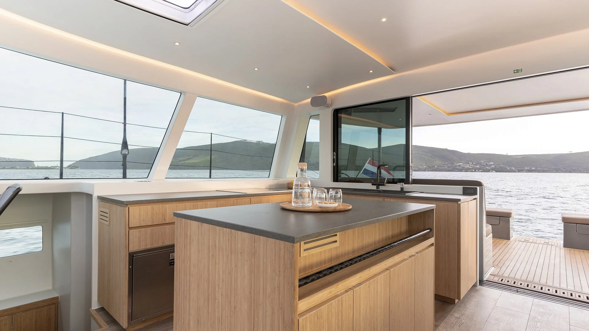 Kinetic Catamarans KC54. Semi custom all carbon performance luxury cruiser. Modern yacht interior with wooden cabinetry and panoramic windows overlooking the sea.