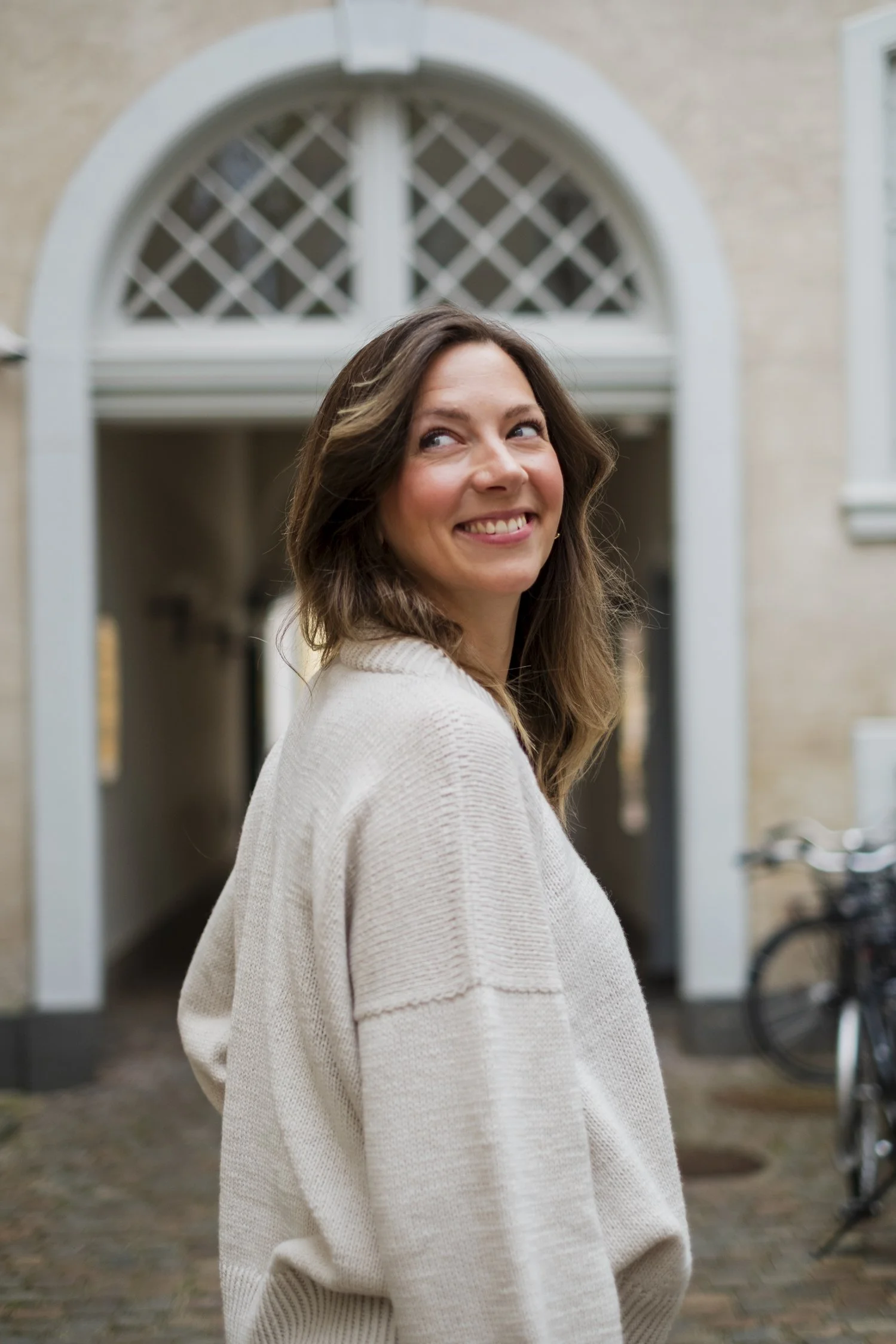 Kika smiling, wearing the cream-colored Simple Things Sweater made with Knitting for Olive merino yarn.