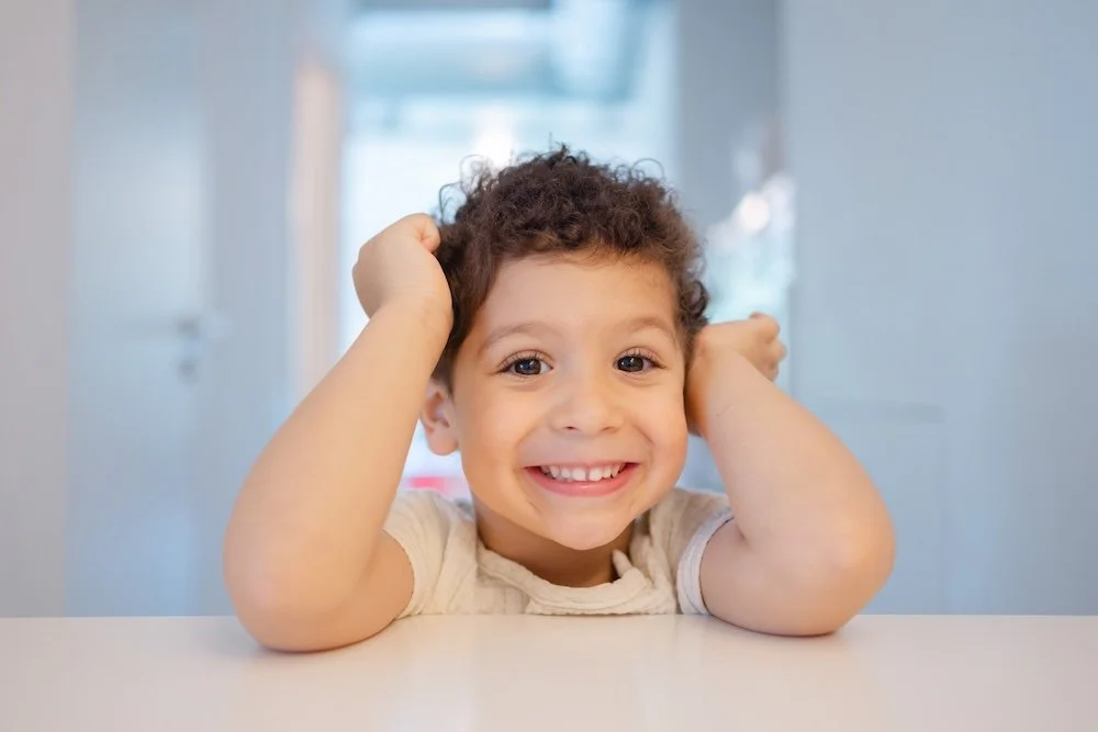 Un garçon souriant avec des bras derrière la tête dans un intérieur lumineux.