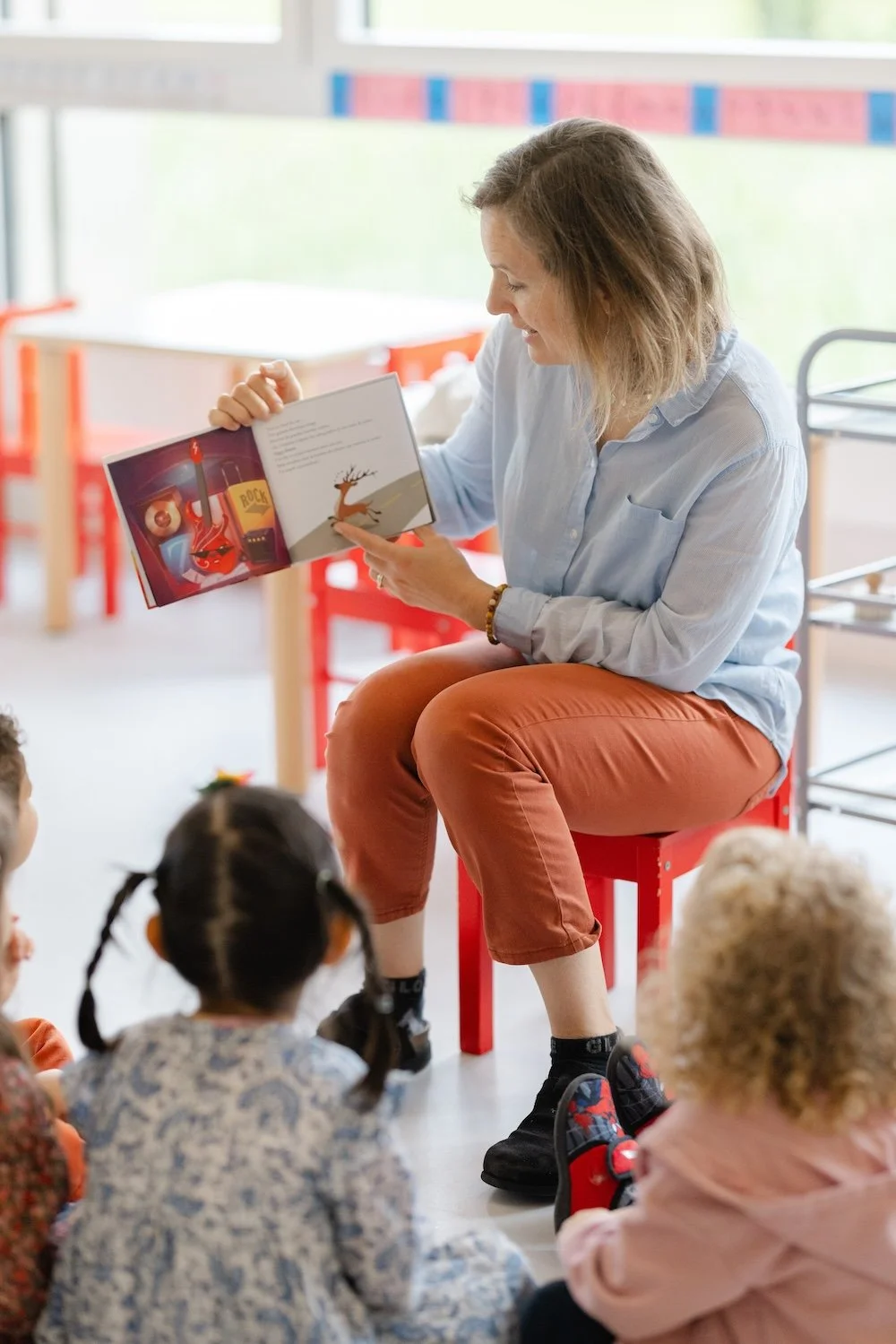 Une femme lit un livre à un groupe d'enfants assis par terre dans une classe.