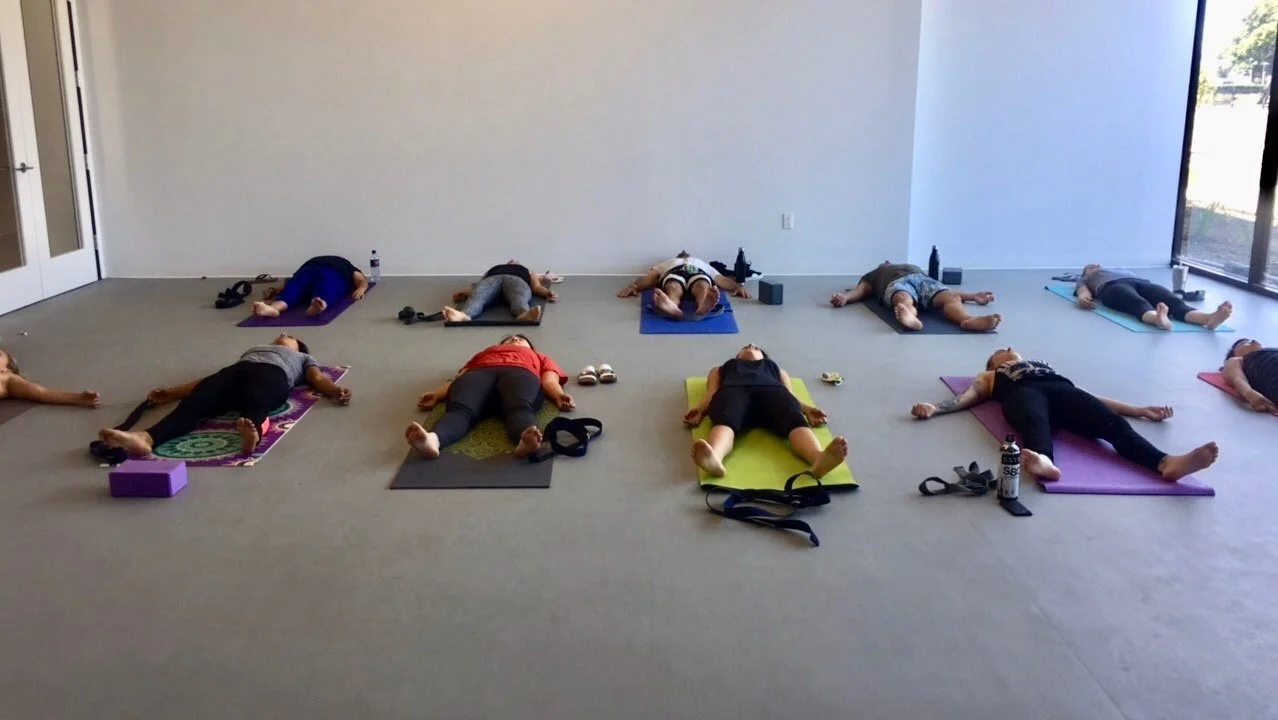 A large group of people laying in corpse pose on their yoga mats