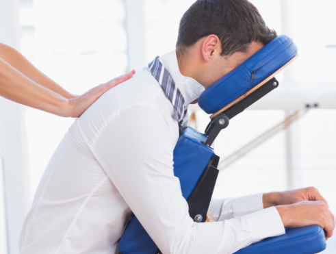 man in white shirt and a blue tie sitting in a massage chair. a massage therapist's hands on his back giving his back a massage