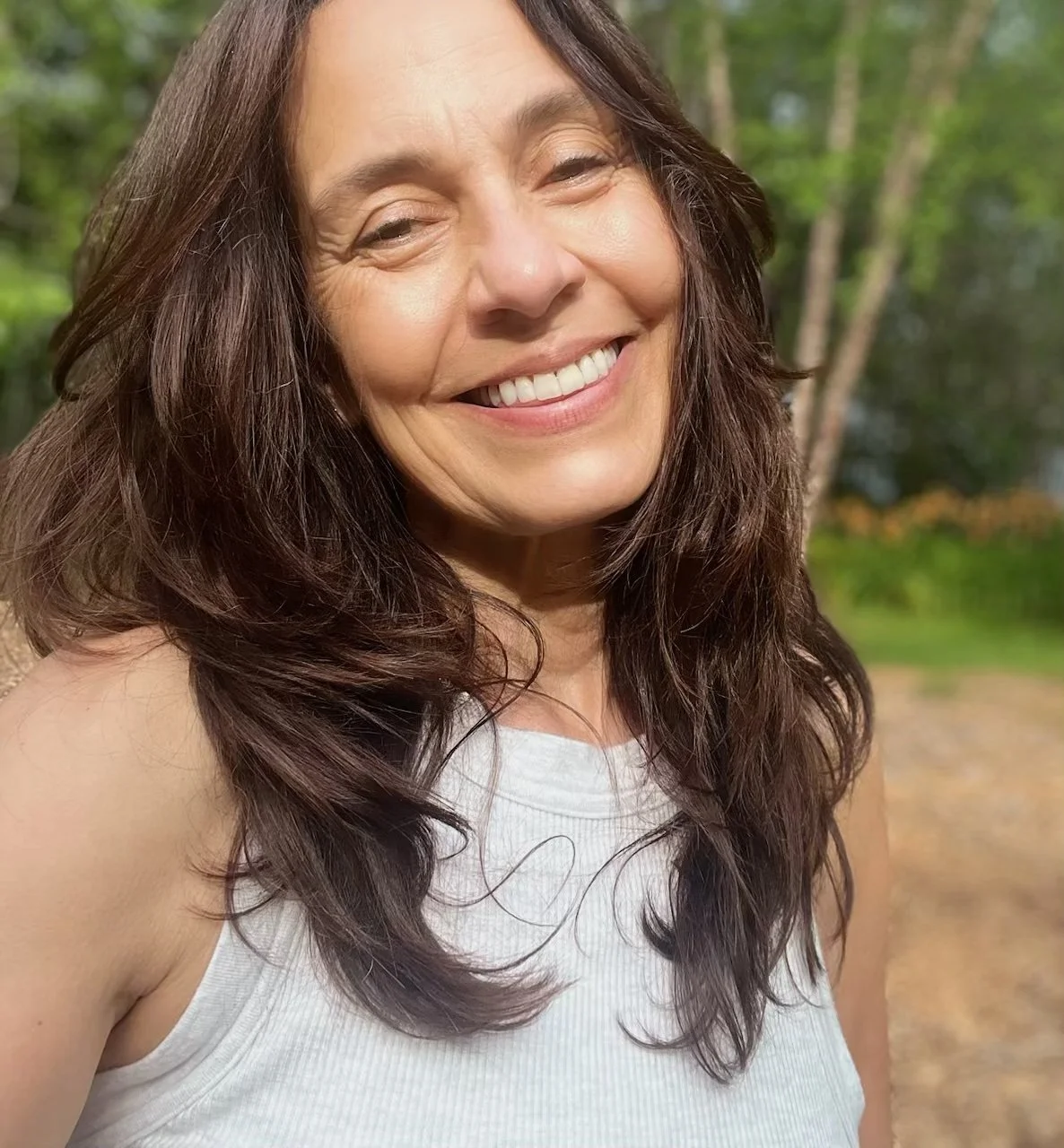 A woman smiling outdoors with trees in the background.
