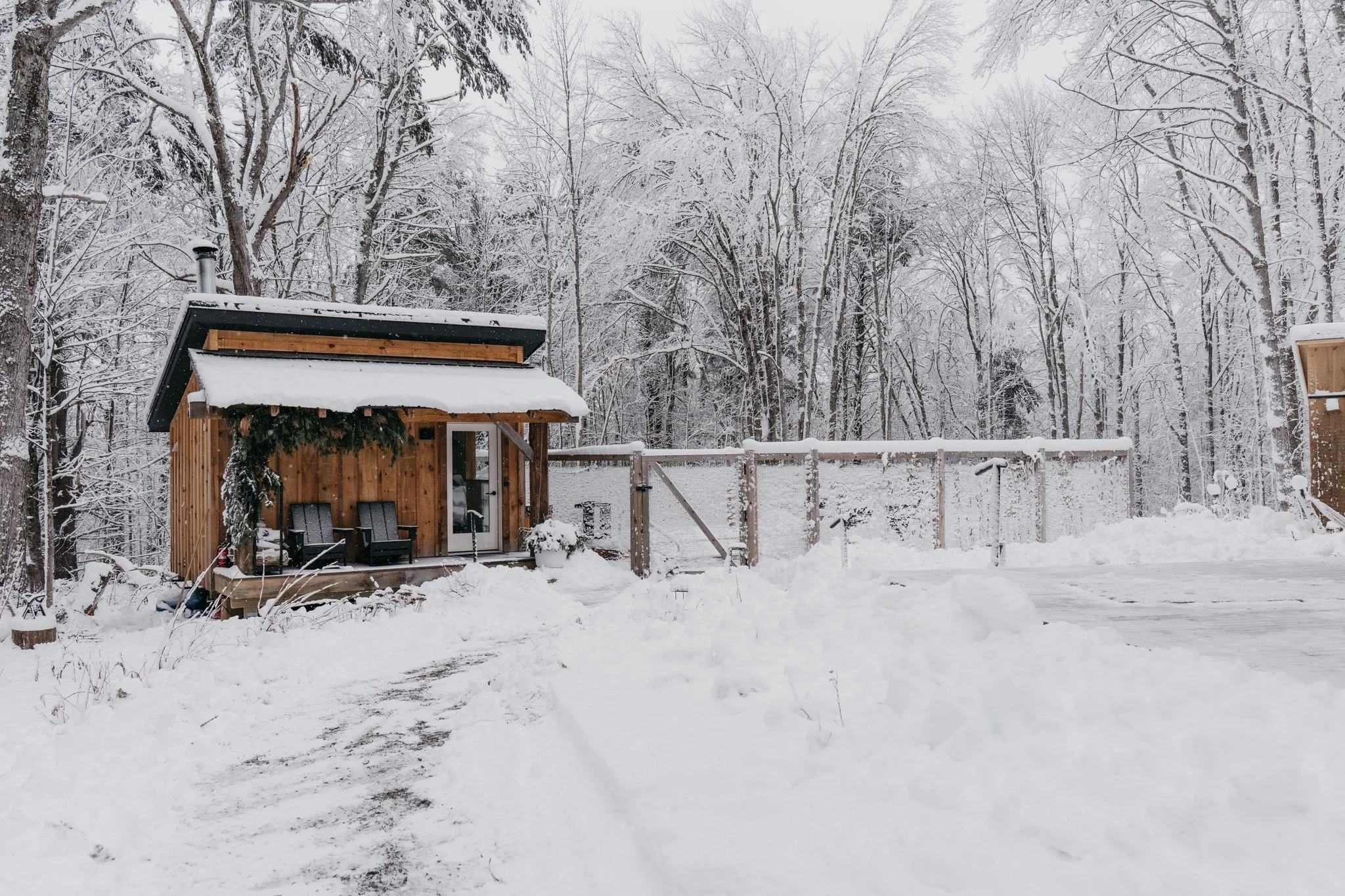 A small wooden cabin with a snow-covered roof, surrounded by snow and trees in a winter landscape.