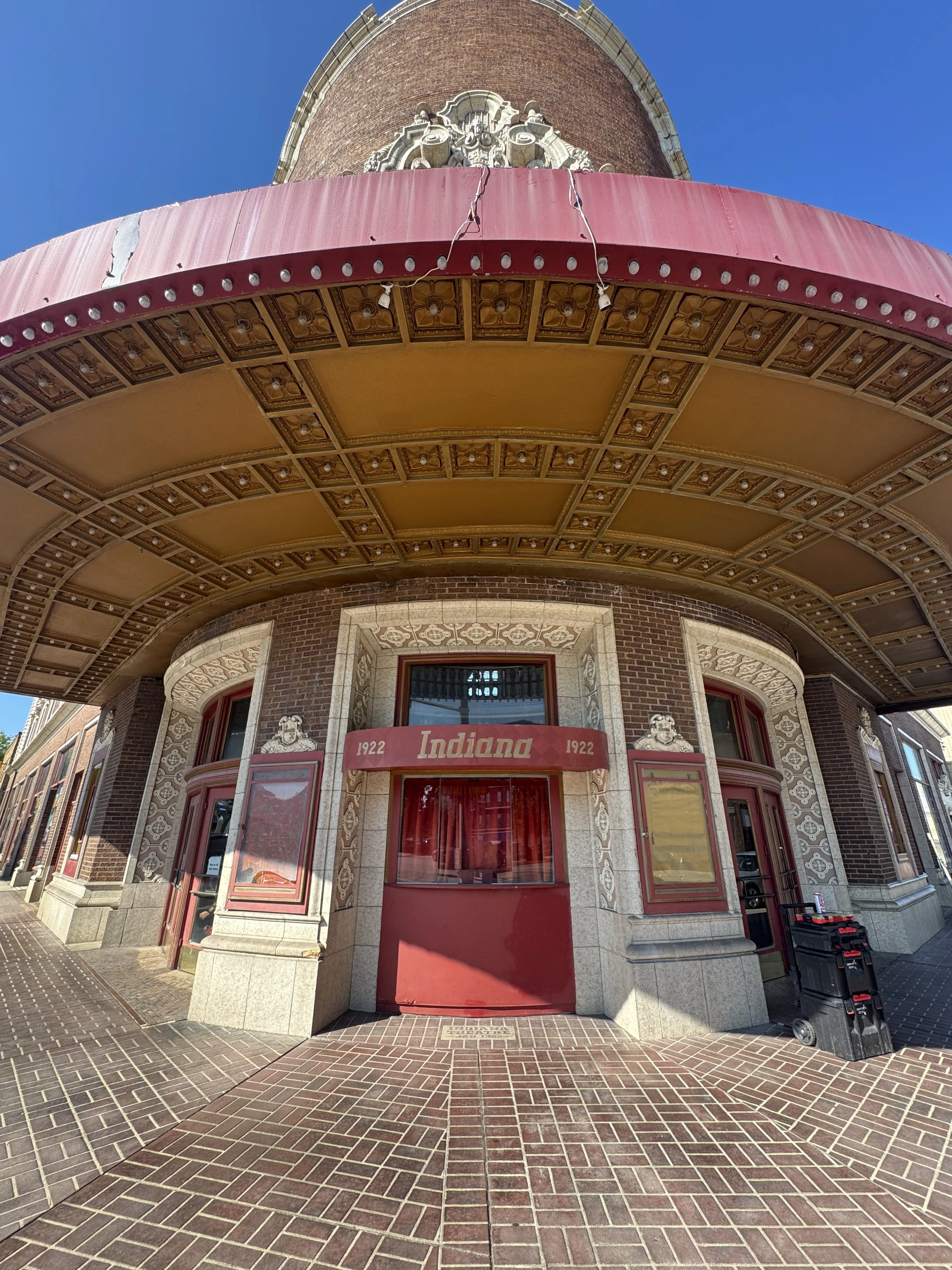 The entrance of a building with a red awning that reads 'Indiana 1922'. Decorative brickwork surrounds the entrance, and ornate detailing is visible above the archway.