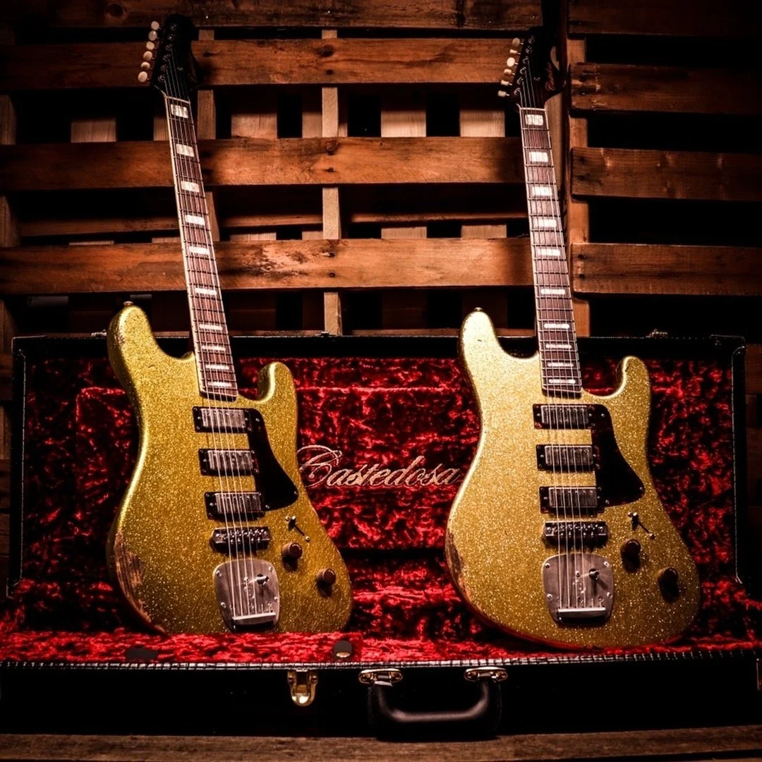 Two gold glitter electric guitars in a red velvet-lined guitar case, set against a wooden background.