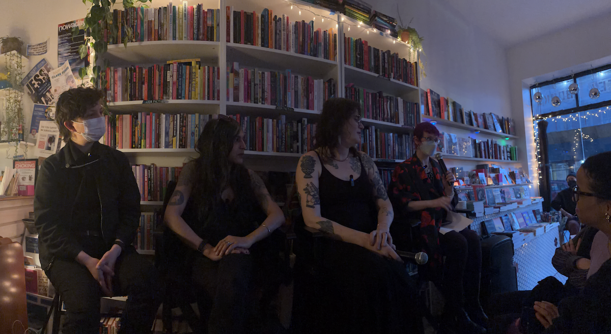 A photograph of four people: E.T. Russian, Rani Som, Mattie Lubchansky, and Margot Atwell, at a bookstore in dim light in front of bookshelves