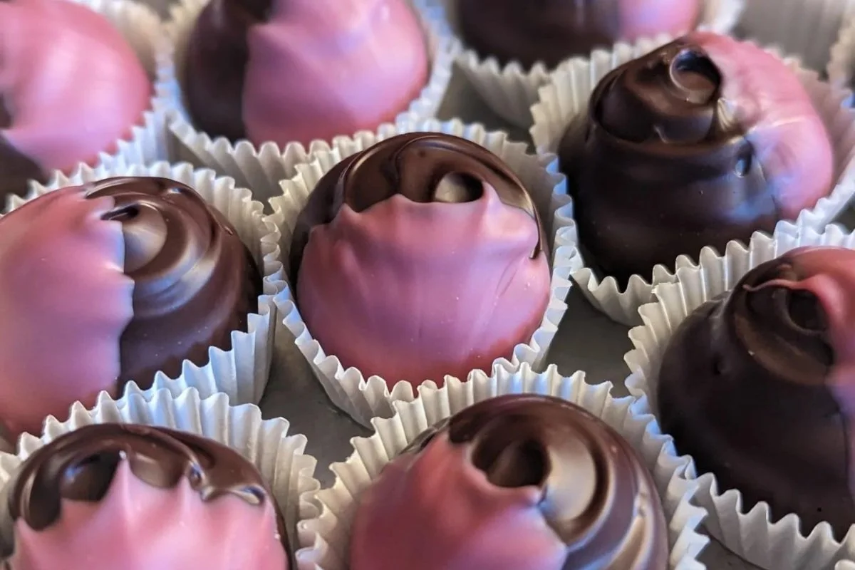 Close-up of assorted dark and ruby chocolate truffles in white candy cups.