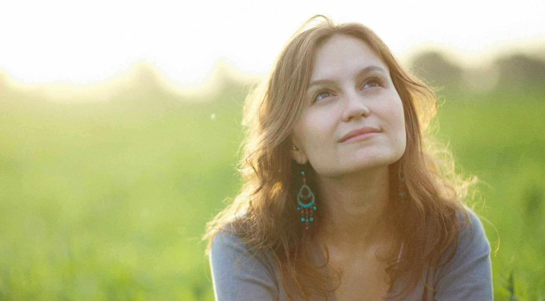 woman sitting in field of grass and looking up at sky