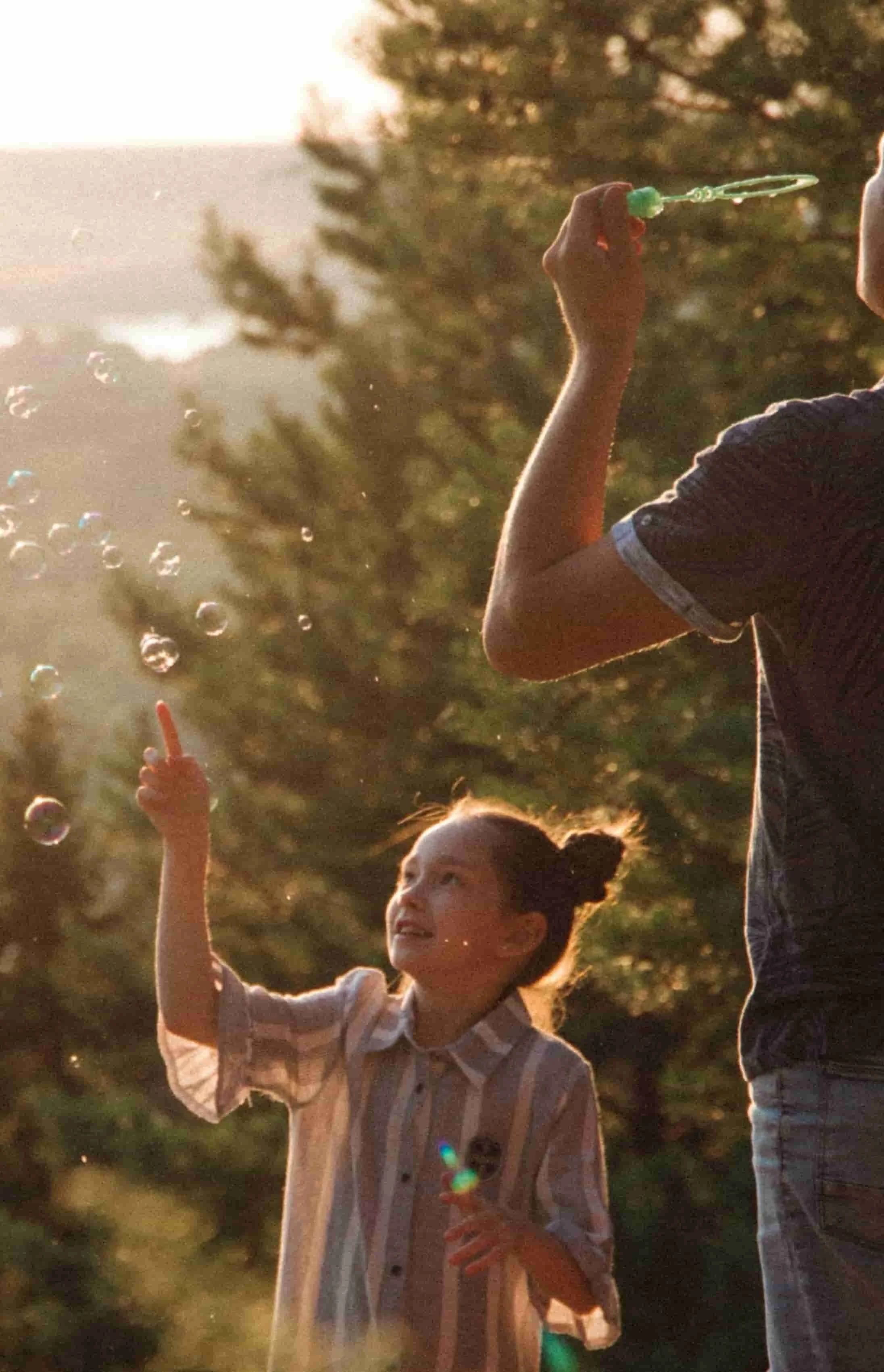 little girl poking bubbles while dad blows them in the forest