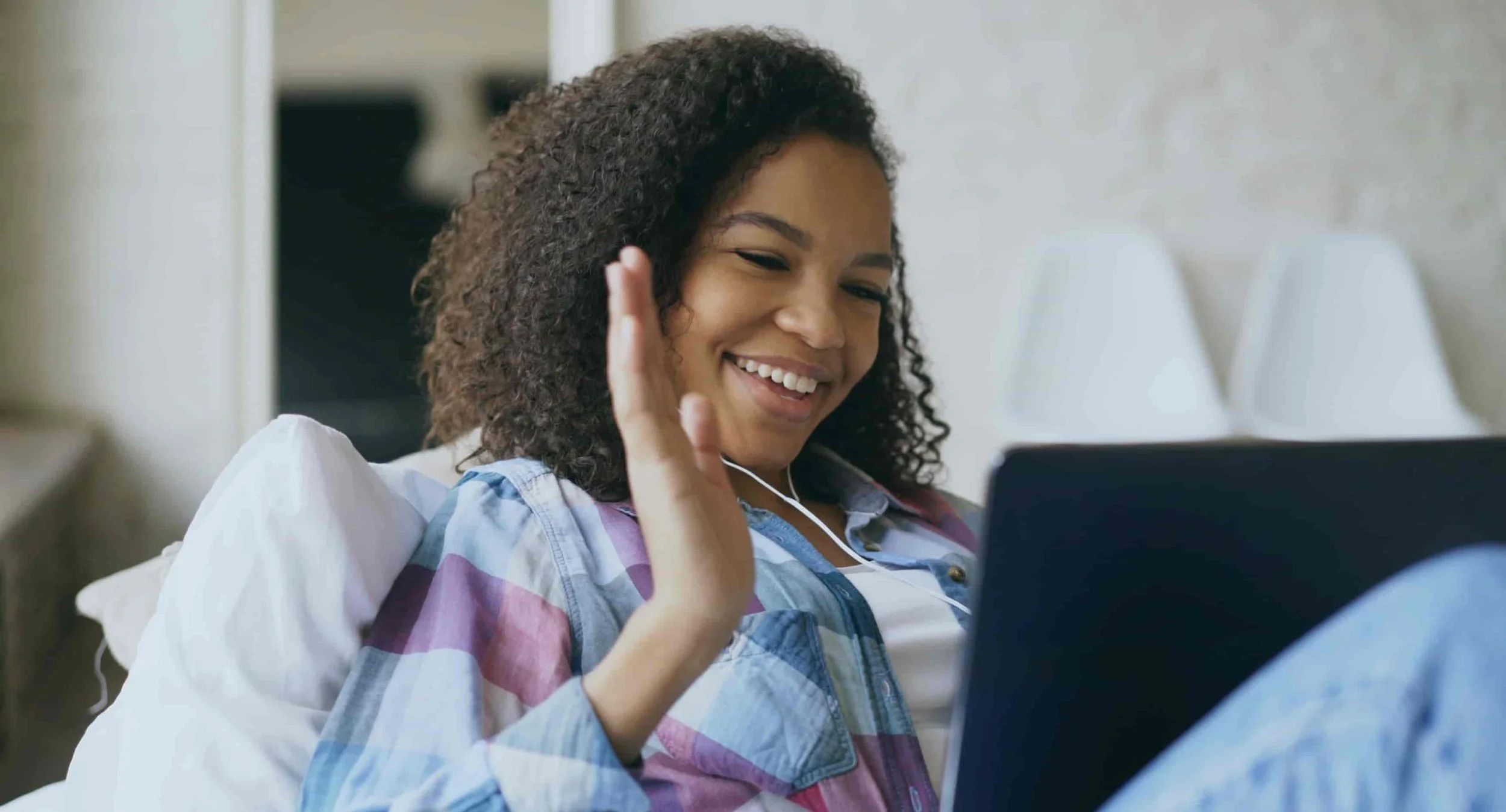 girl sitting on couch and waving at open laptop while on video call