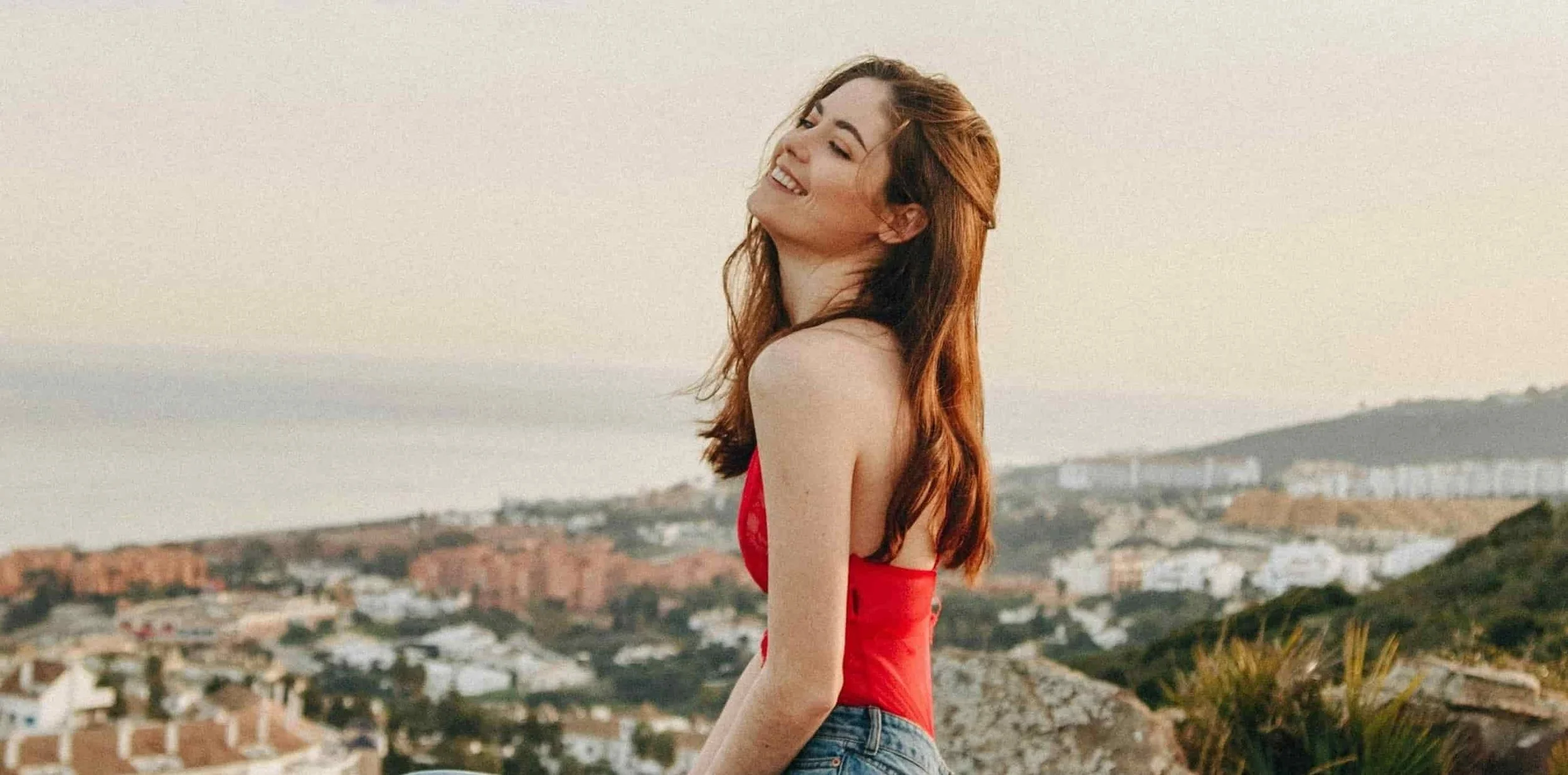 woman sitting on rock with city outline behind her