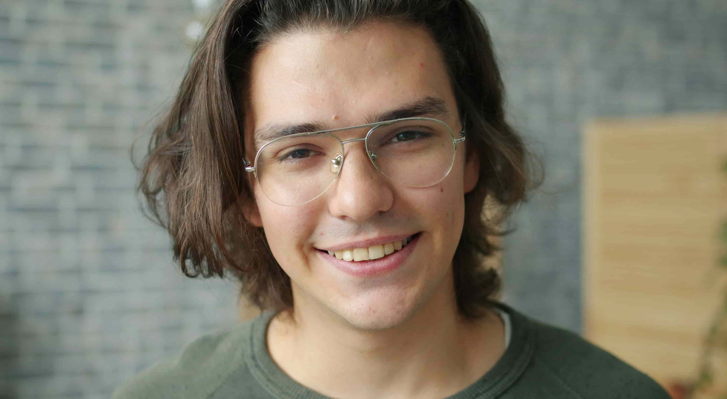 man with shoulder length hair and glasses smiling at camera