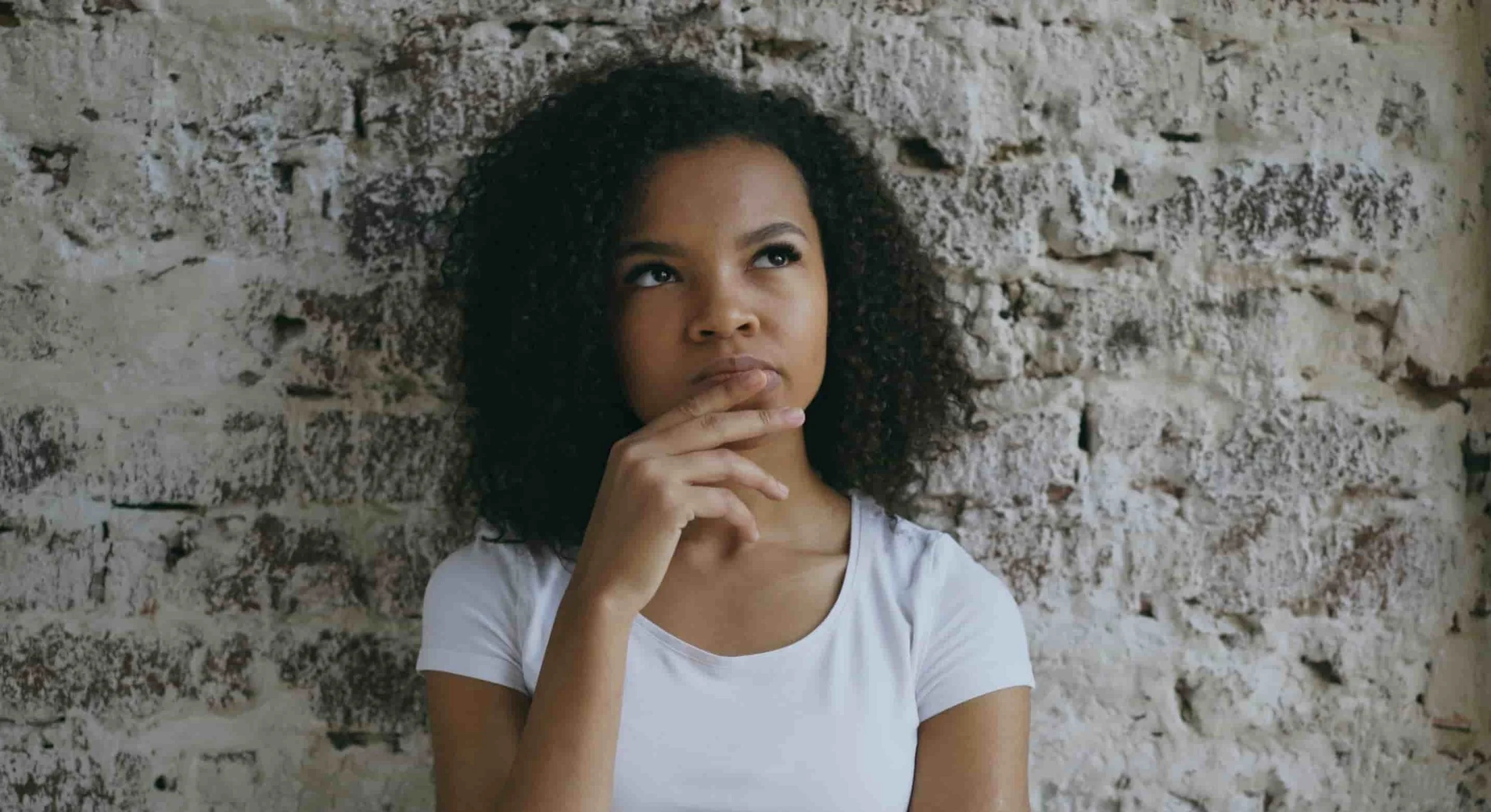 girl leaning against wall with hand on chin thinking