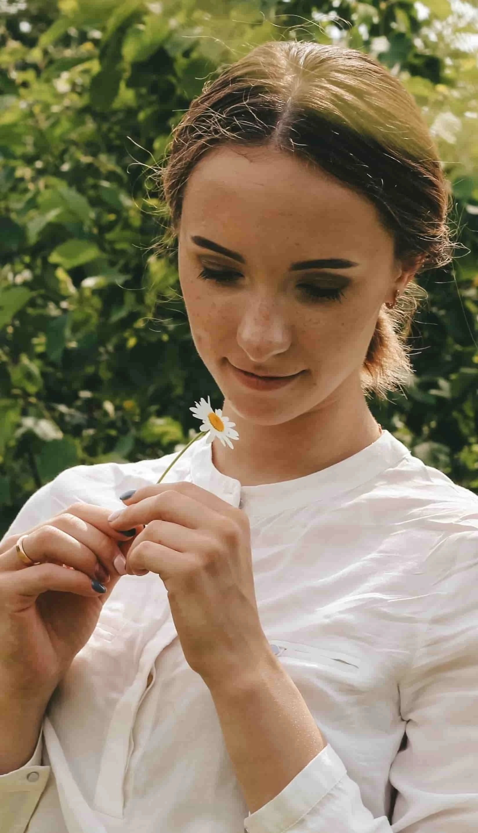 woman staring down at daisy in hand