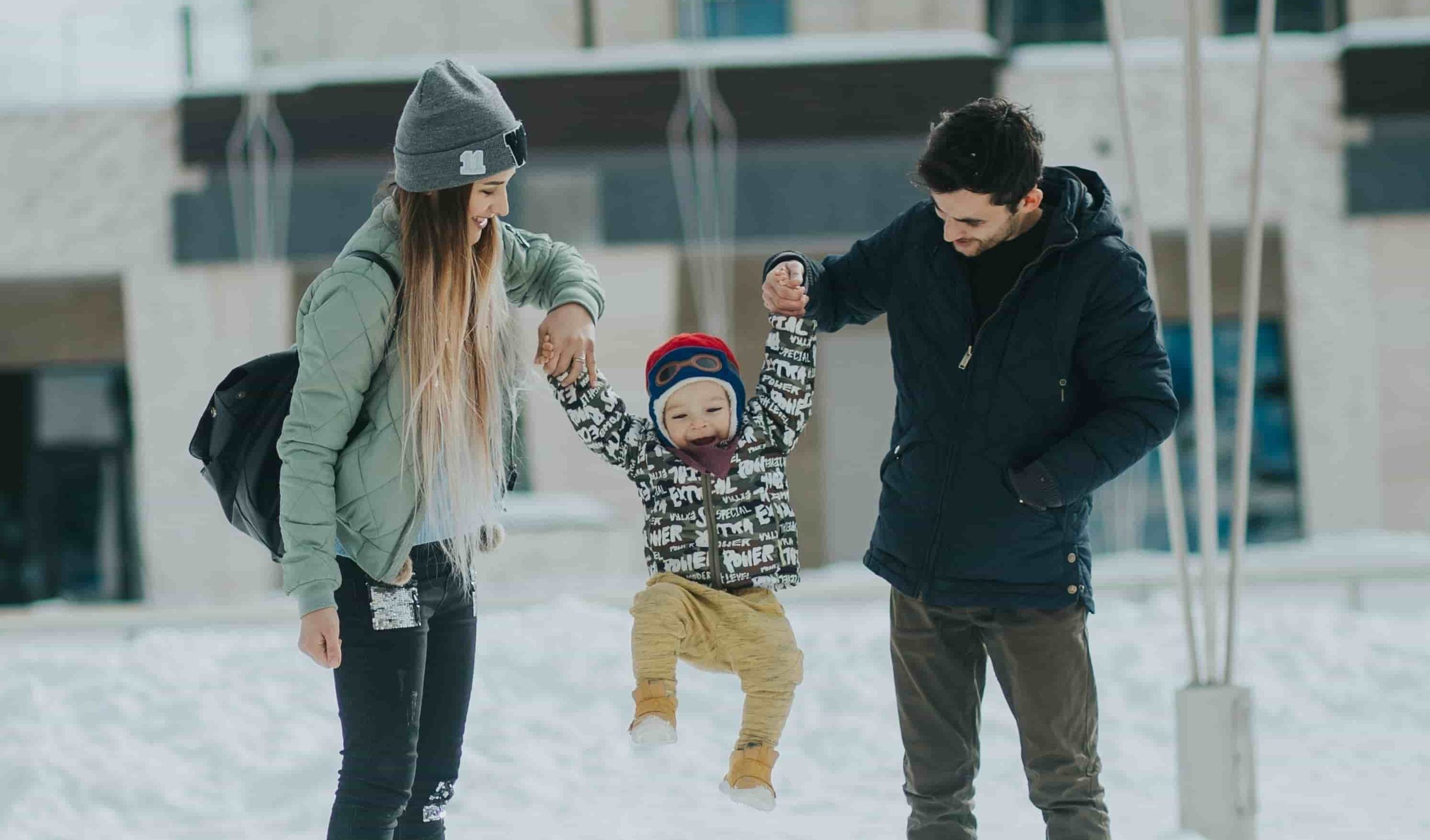 mom and dad holding son's hands while swinging him