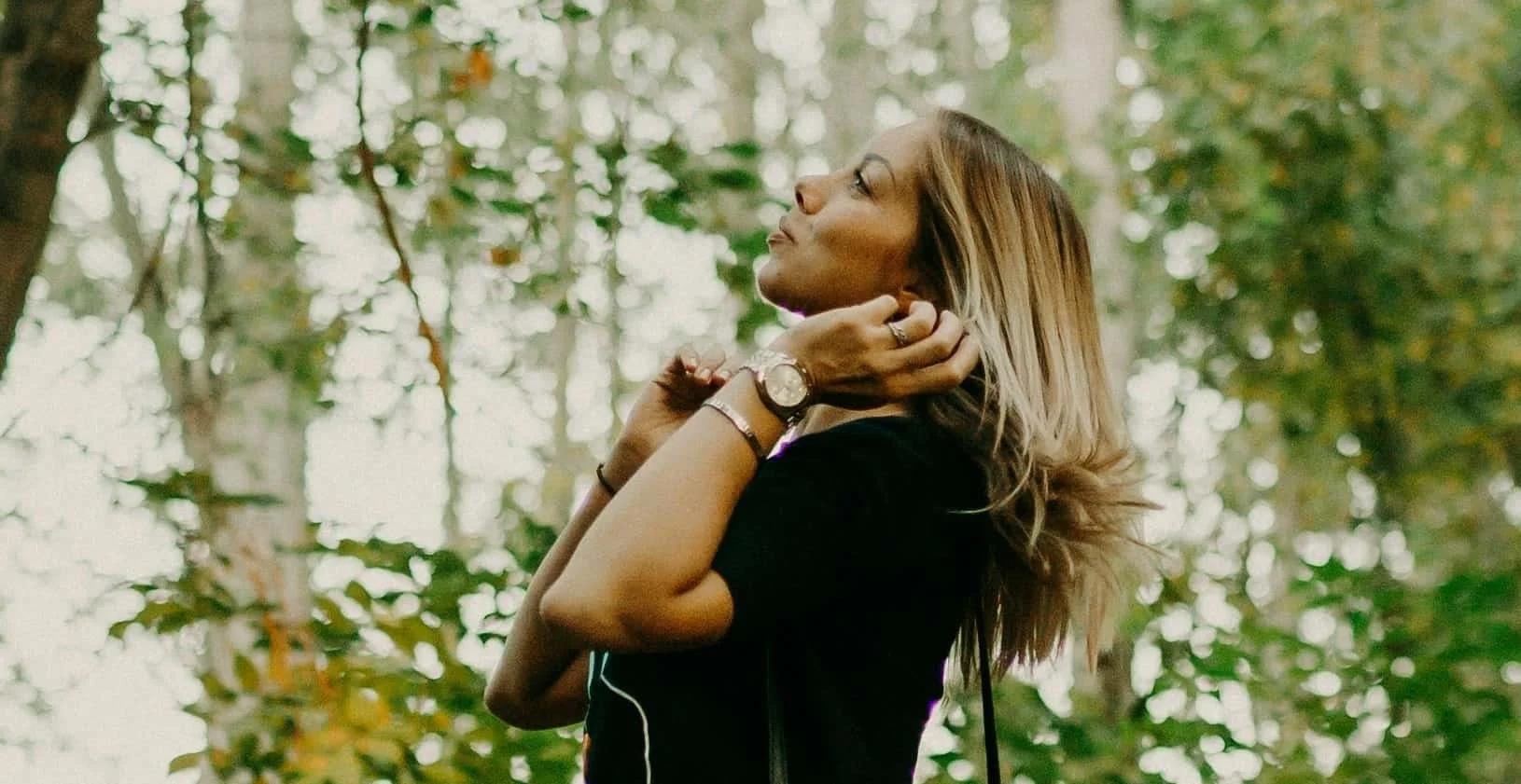 woman looking up while standing in forest
