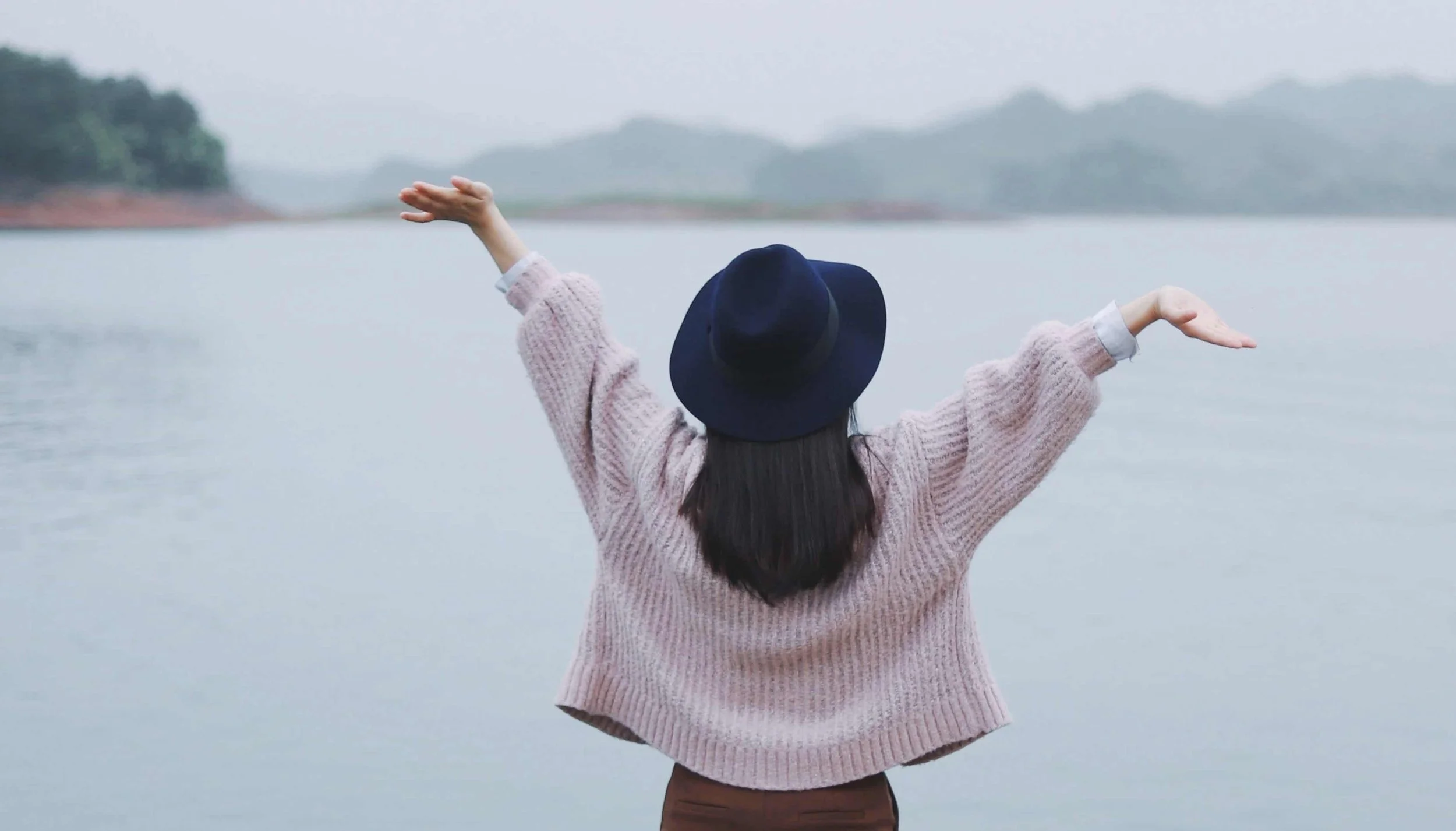girl with her hands in the air on the edge of a bridge near the ocean