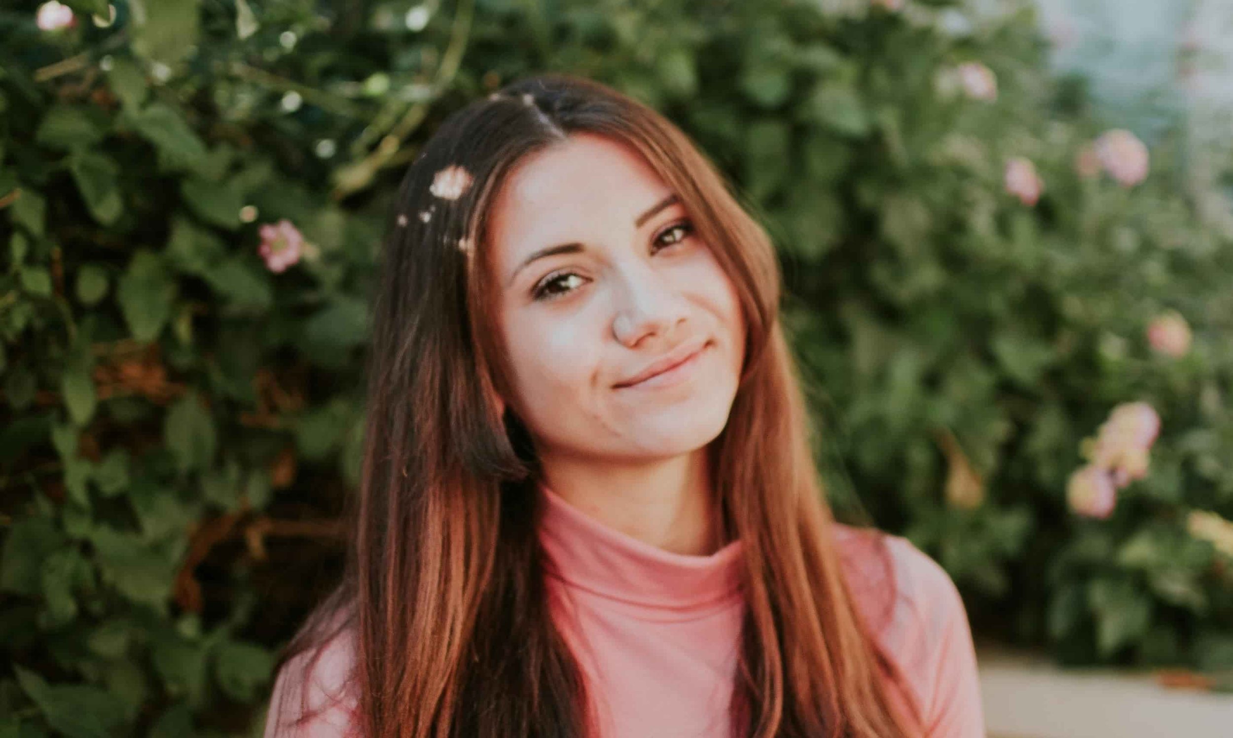girl sitting in front of pink rose bush and smiling at camera