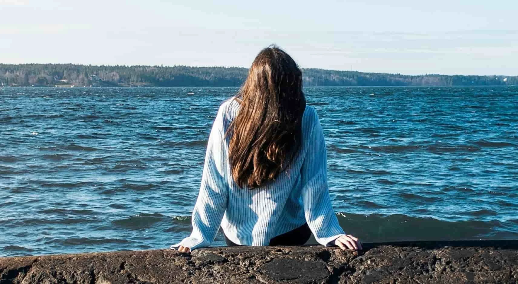 woman sitting on rocks, staring at the ocean