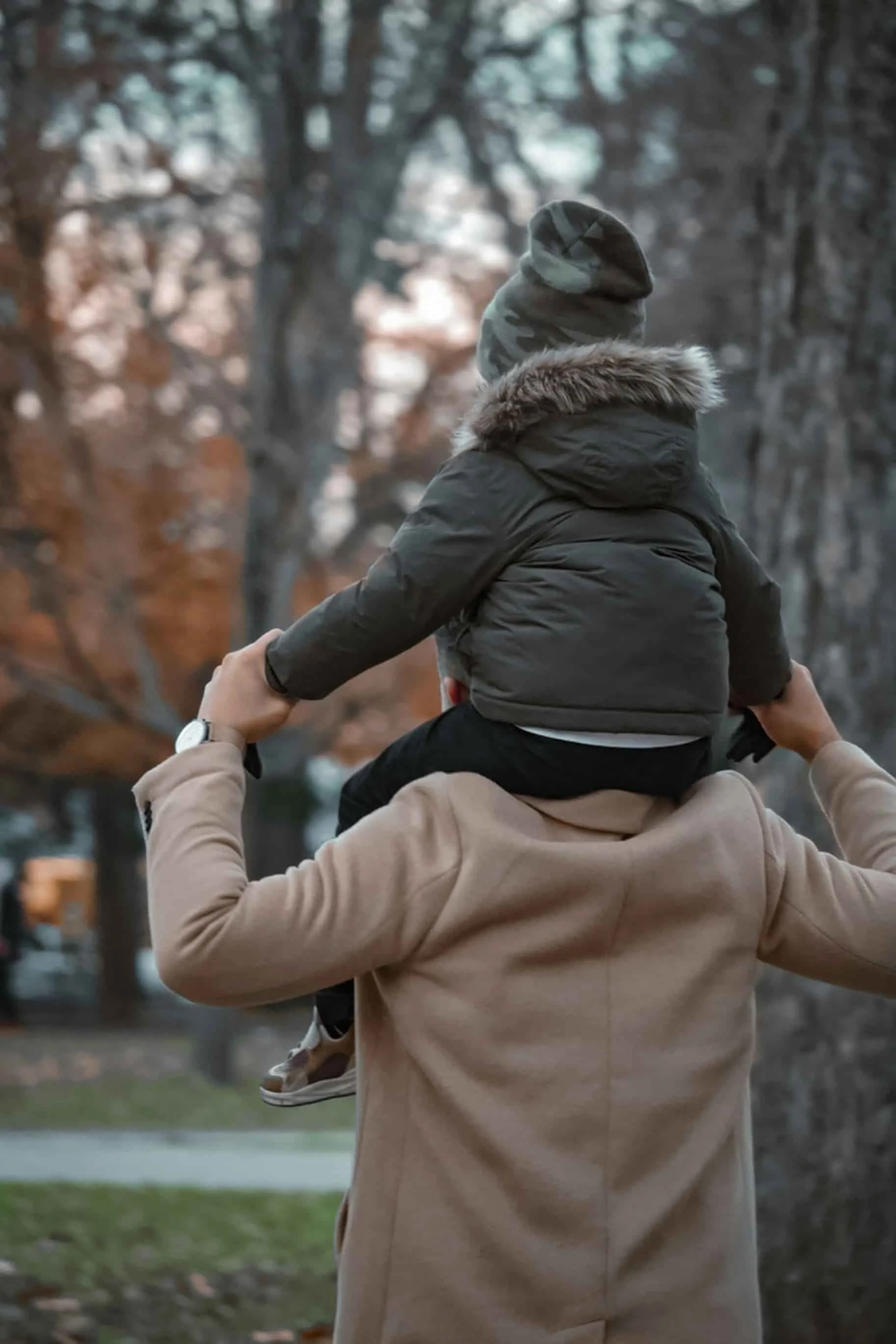 father carrying son on shoulders in park