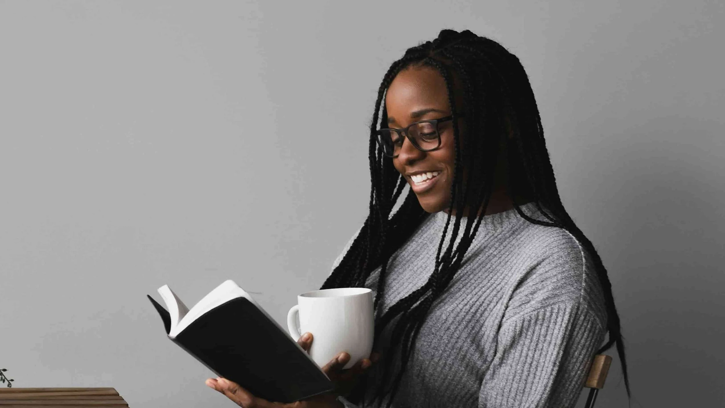 girl sitting at table with a cup of coffee and reading a book