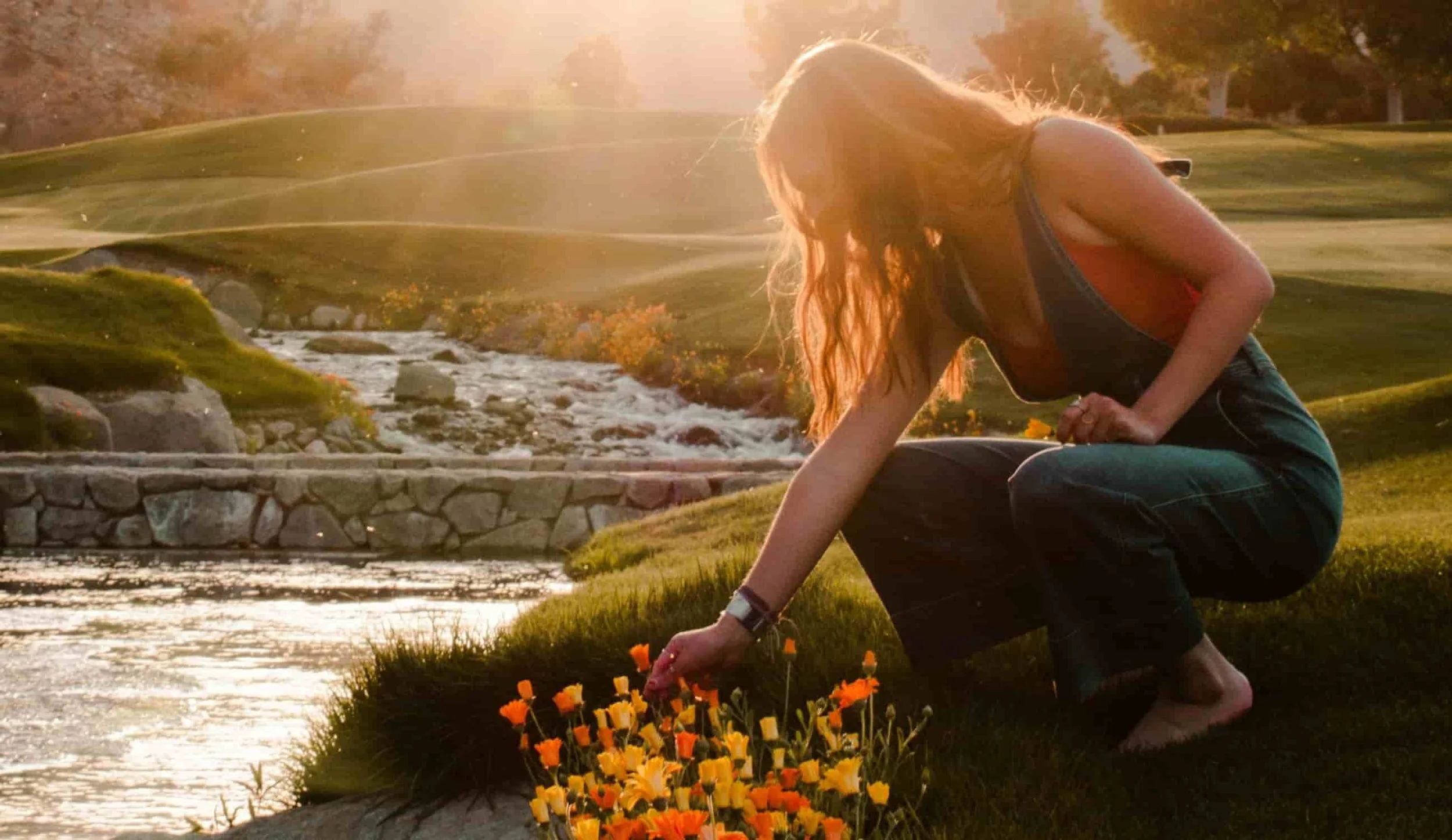 woman picking orange and yellow flowers by lake