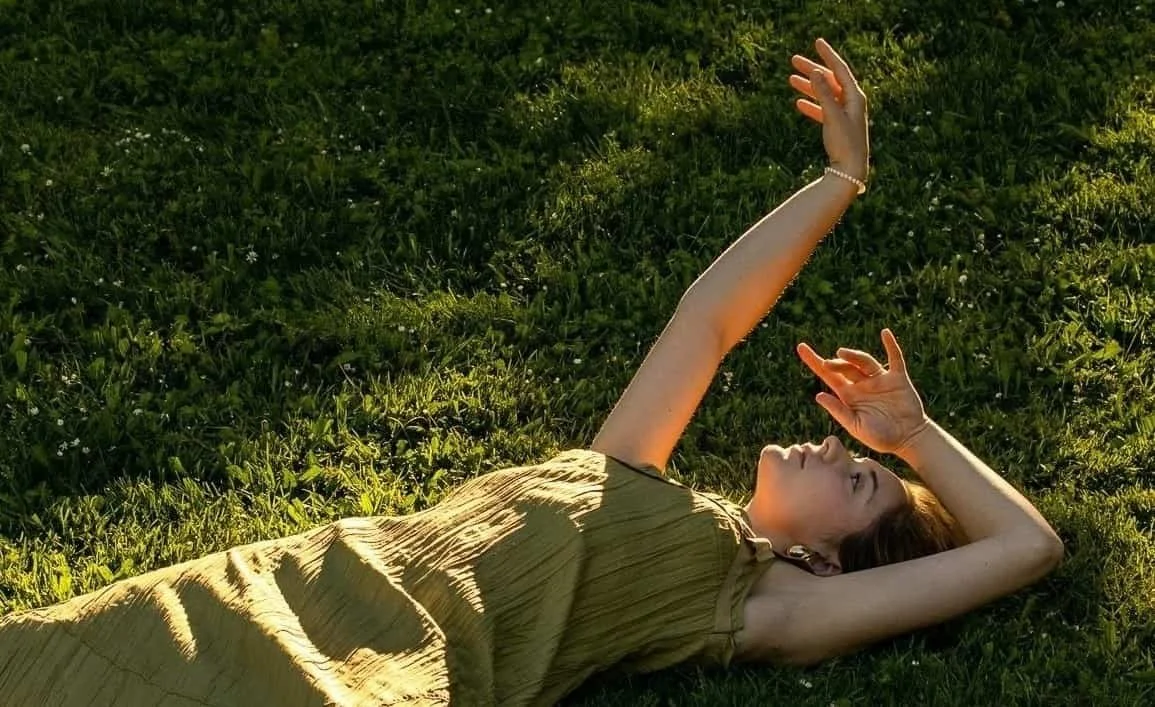 girl laying in grass while looking up at the sun