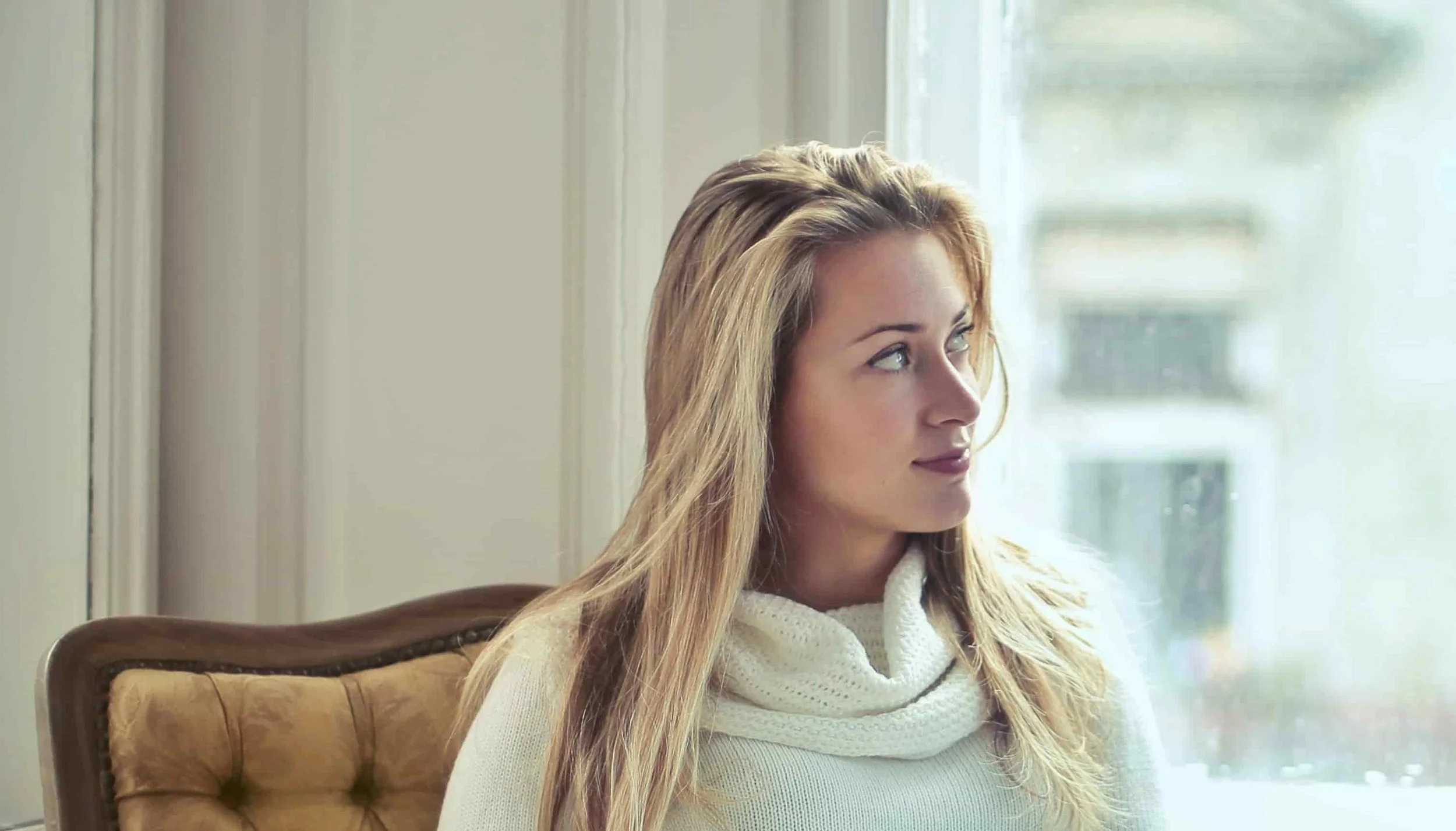 woman sitting on a yellow couch while looking out the window