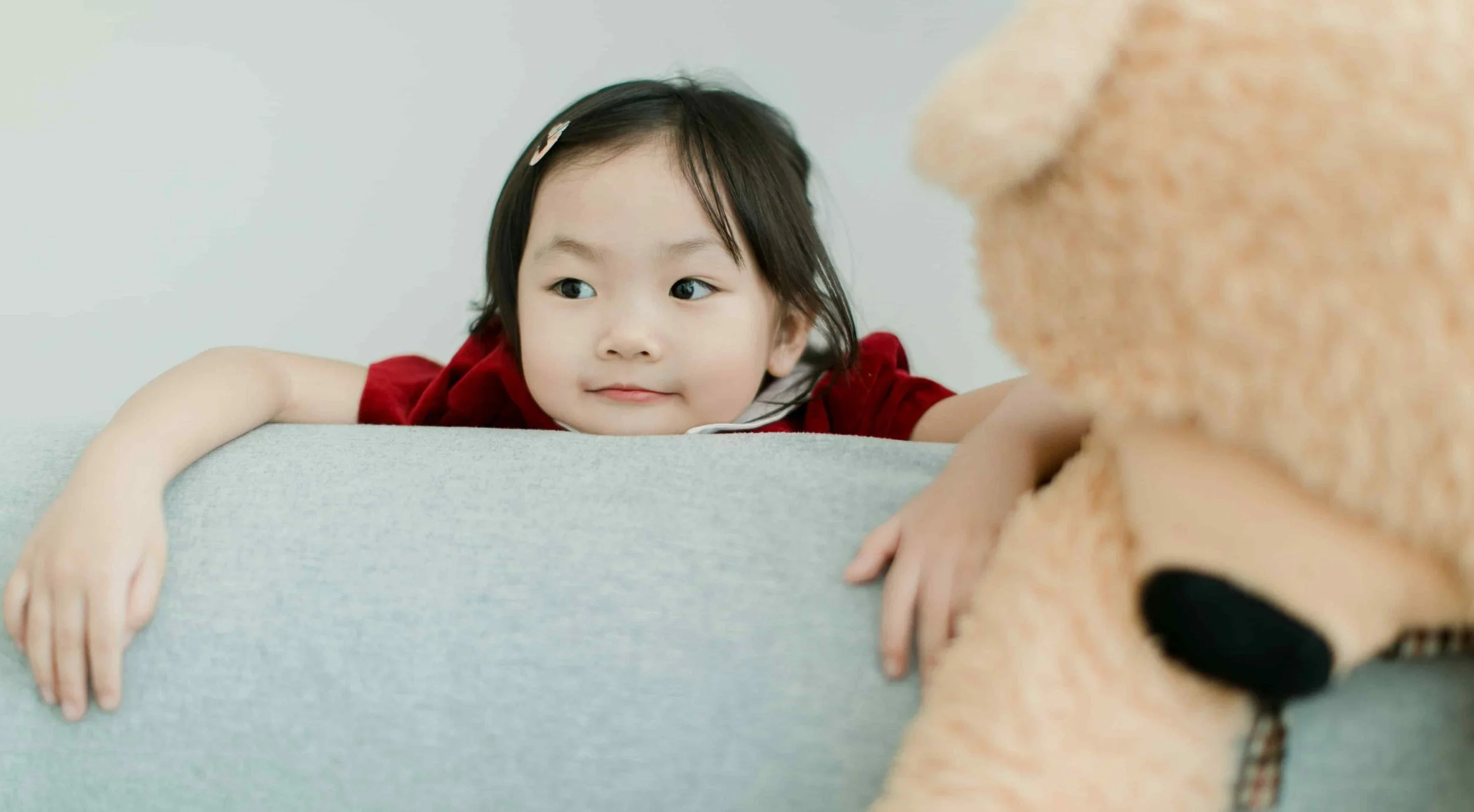 child leaning head on sofa cushion next to teddy bear