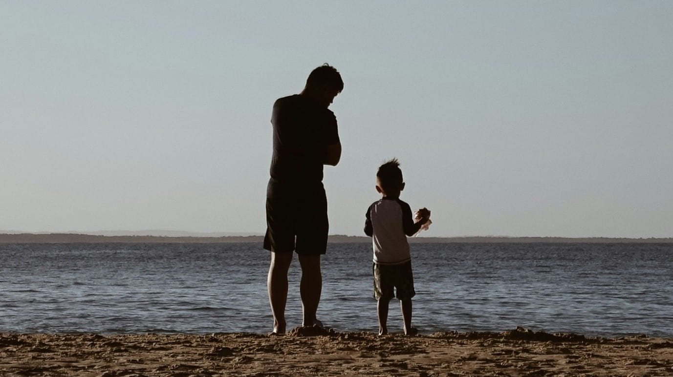 dad and son standing on sand the beach and looking at the ocean