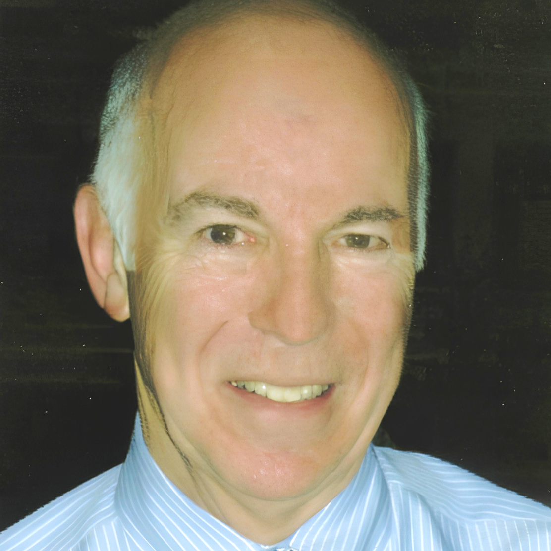 Close-up of a smiling middle-aged man with short, light-colored hair, wearing a blue striped shirt.