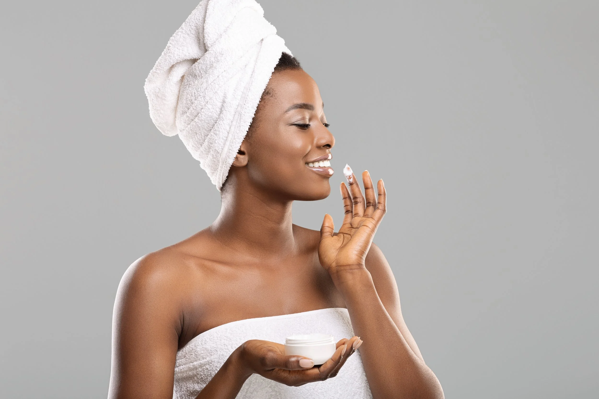 Woman placing CBD skincare lotion on face while holding jar