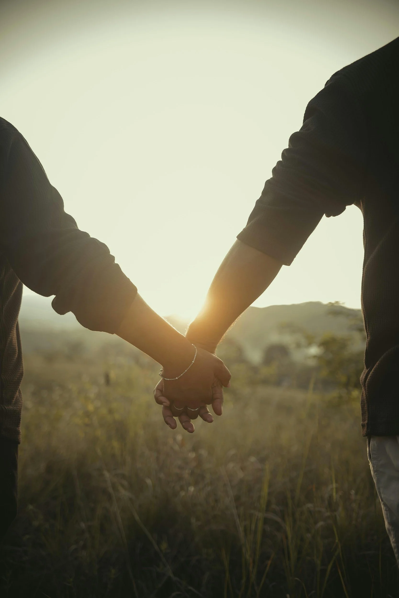 Two people holding hands in a field at sunset, LGBTQ+ affirming therapy in NYC