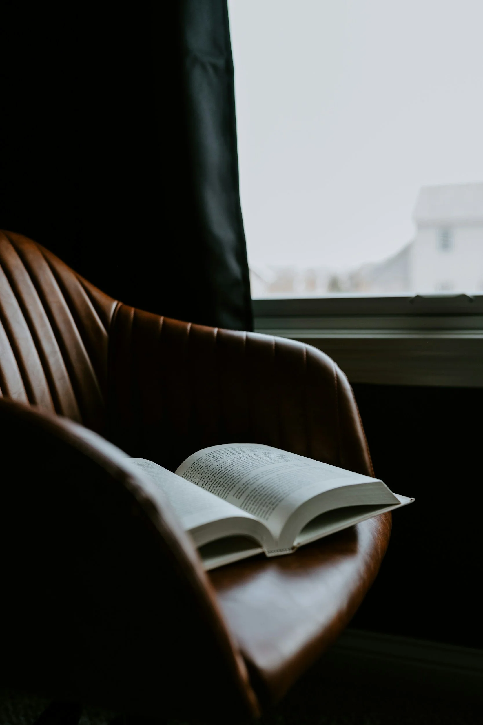 Open book resting on a leather armchair by a window, therapy for high achievers in NYC