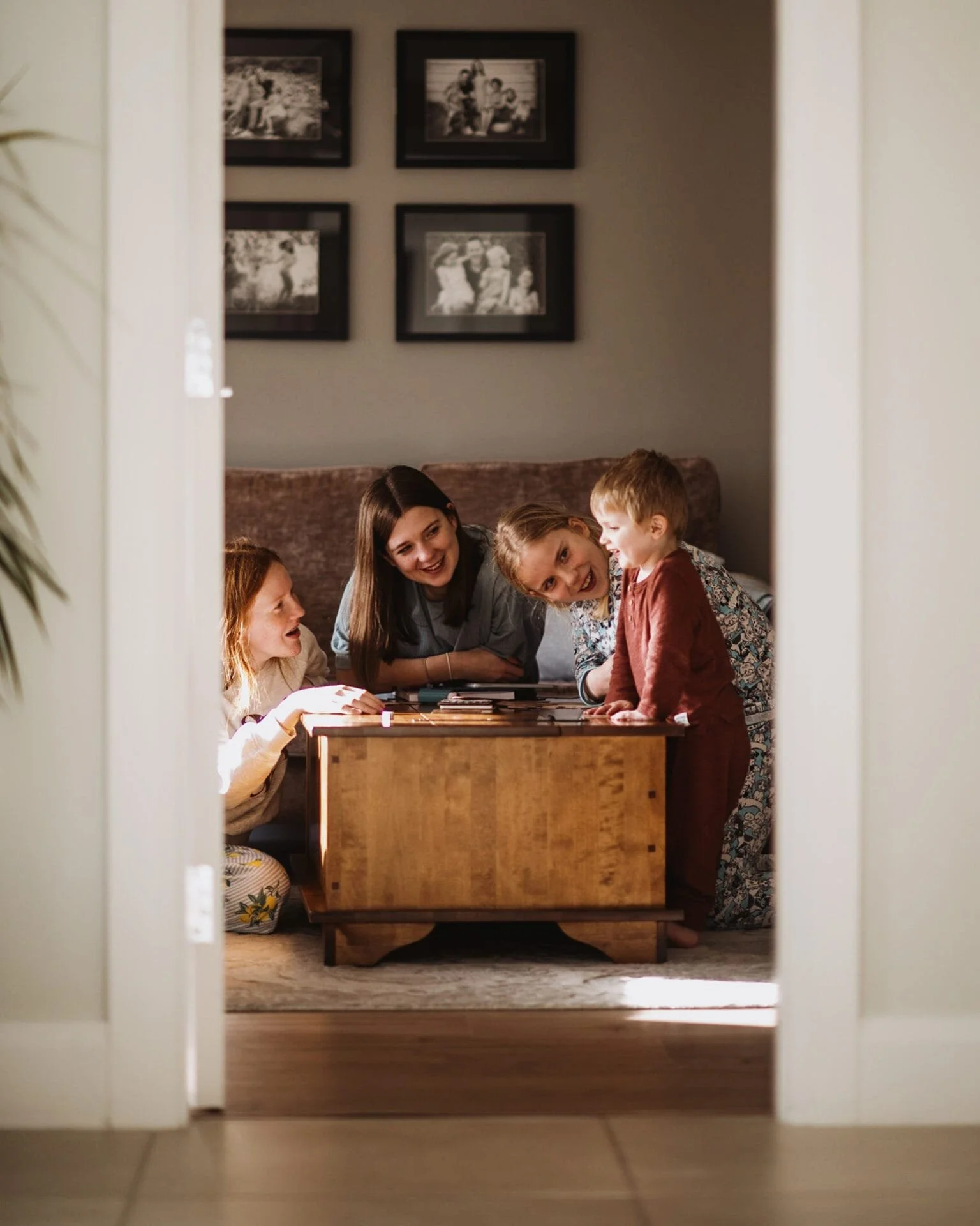 Children and a woman playing a game or doing an activity at a table, viewed through a doorway.