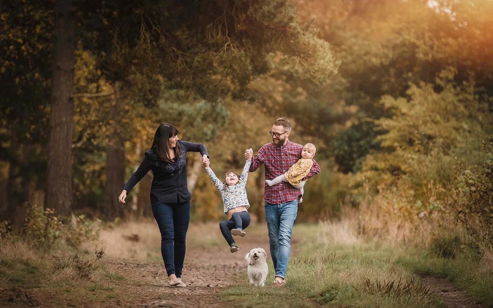 A family of four, with two children and a dog, walking on a forest trail during fall, enjoying their time together.