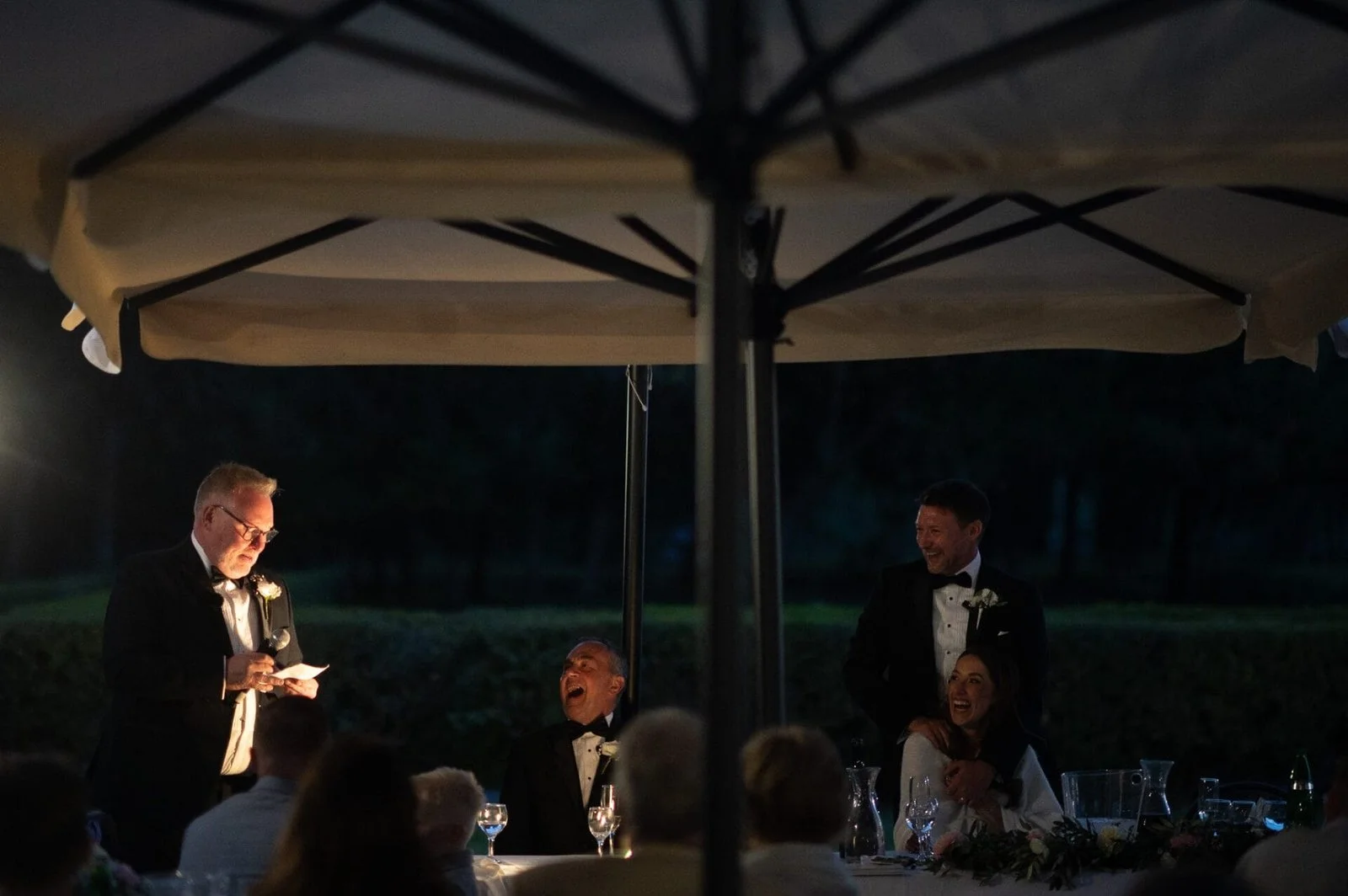 outdoor evening speeches at Rome wedding. 3 men n tuxedos and the bride all smiling and laughing