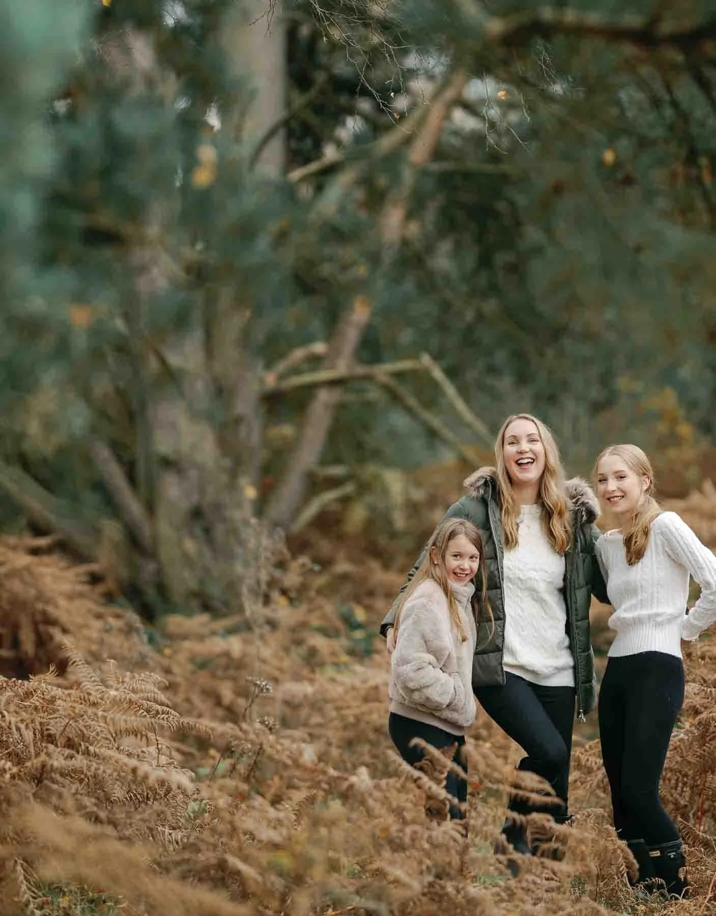 mother and 2 young daughters laughing in autumnal park setting