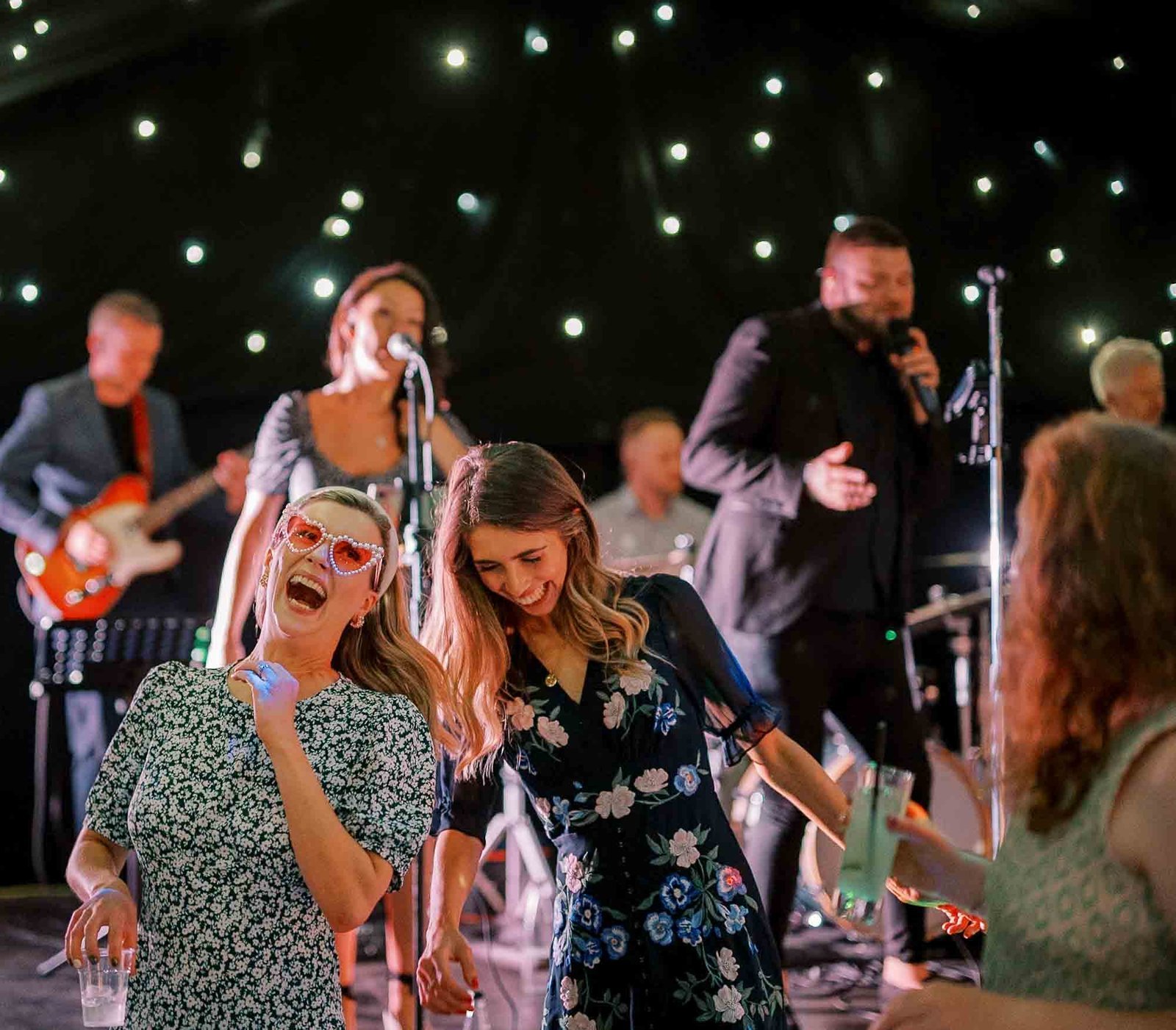 People dancing and laughing at a party with a live band performing on stage in the background. Yorkshire wedding photos