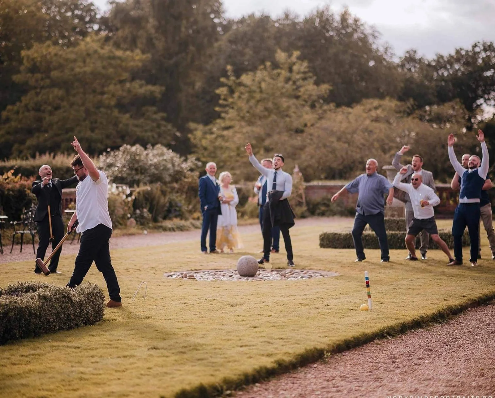 People playing an outdoor lawn game, likely croquet, at a gathering or celebration, with trees in the background. Hodsock Priory wedding photo