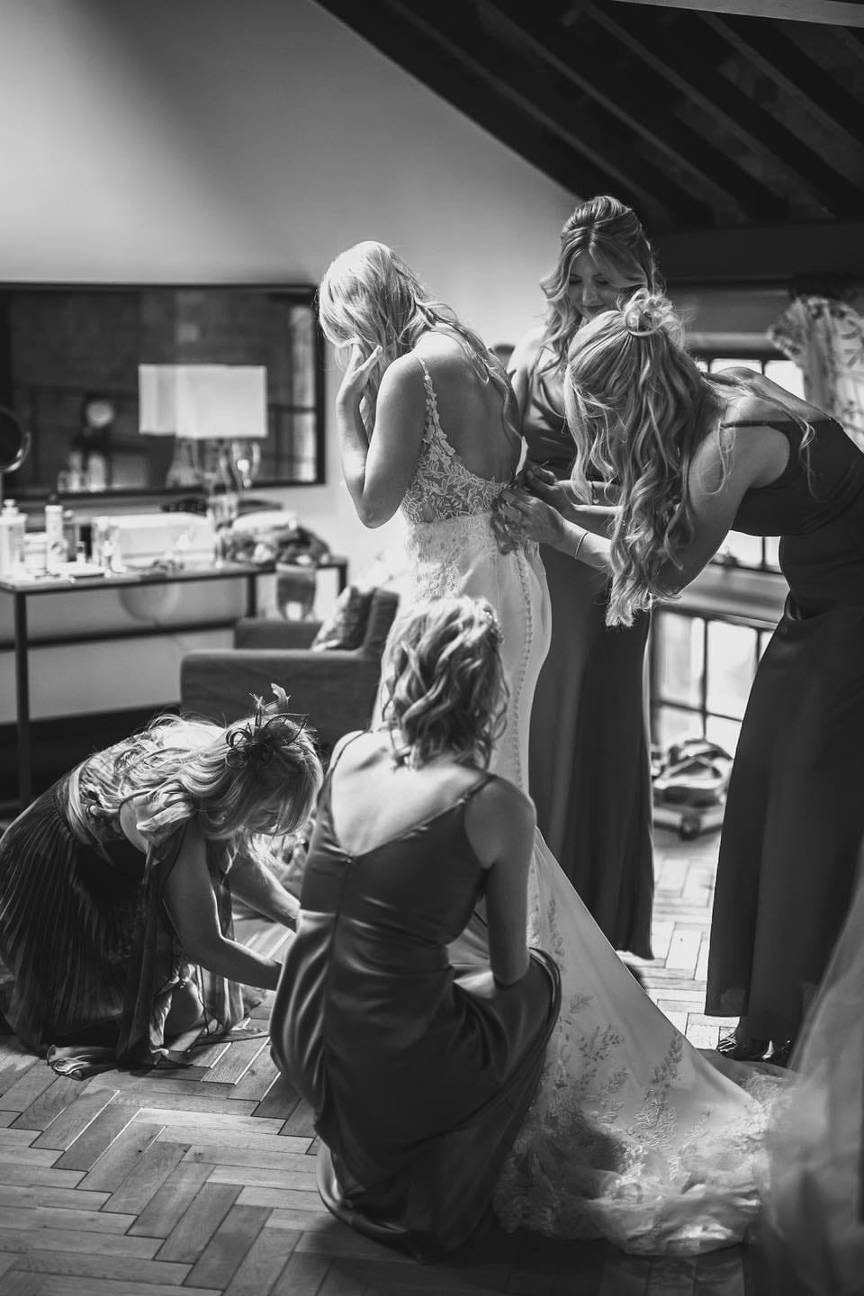 balckj and white photos of a bride and bridesmaids helping her into her wedding dress at ollerton pumping house wedding venue