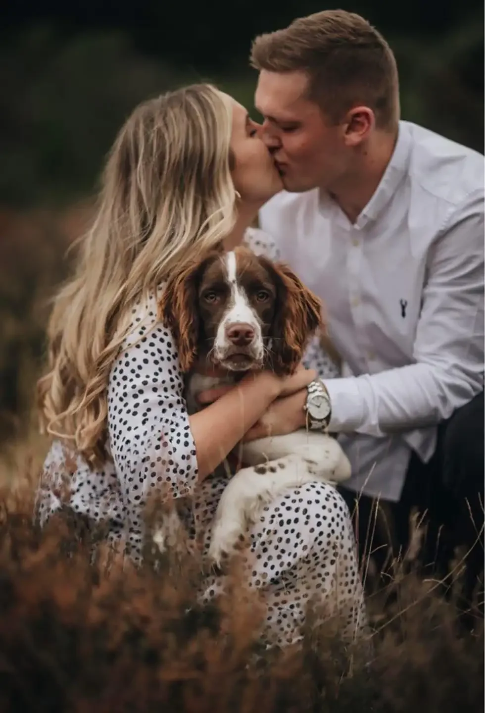 Candid moment of a Springer Spaniel sitting between a kissing couple during an outdoor Yorkshire engagement shoot.