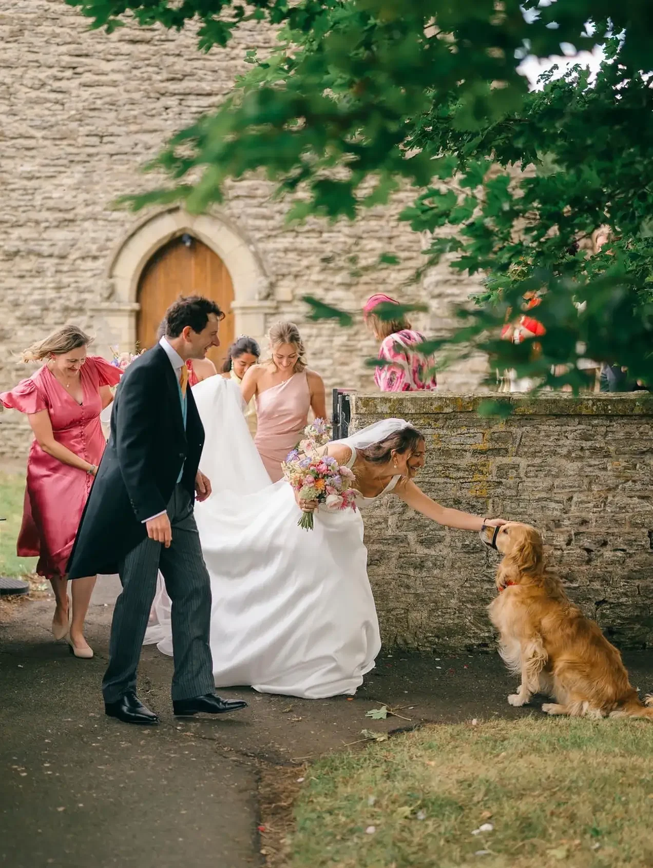 Bride petting a friendly Golden Retriever outside a traditional stone country church in Yorkshire.