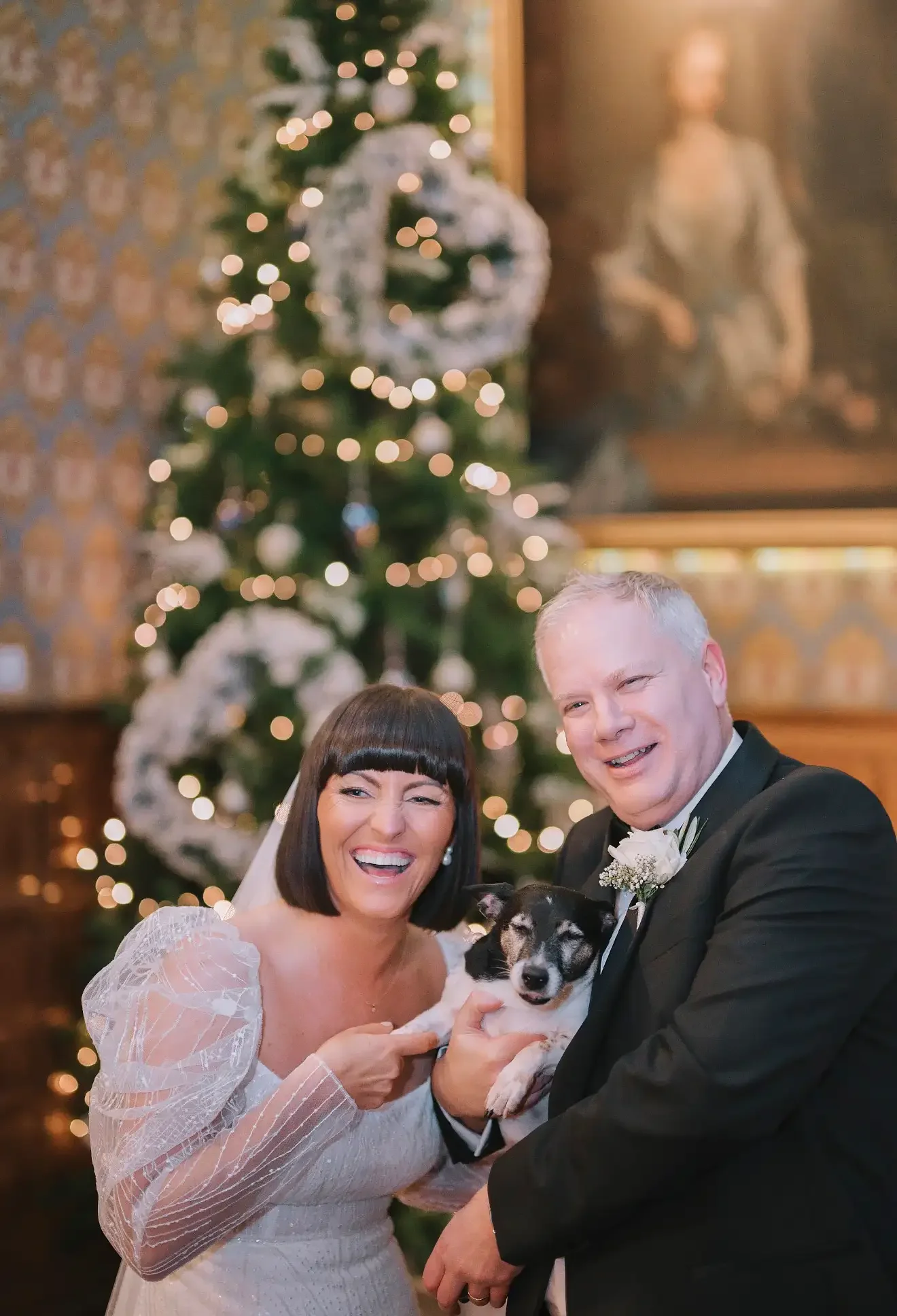 a bride and groom smilng and laughing whilst holding their blck and white small terrier dog. christmas wedding at hodsock priory taken by wedding photographer yorkshire portraits